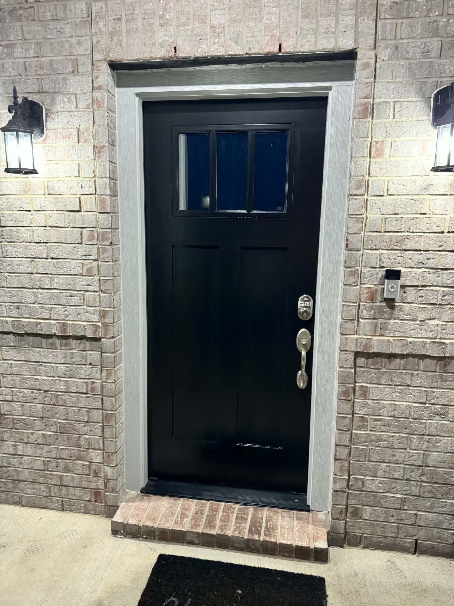 Charming entrance with a sleek black door framed by elegant brickwork and illuminated by stylish lanterns, offering a warm and welcoming first impression.