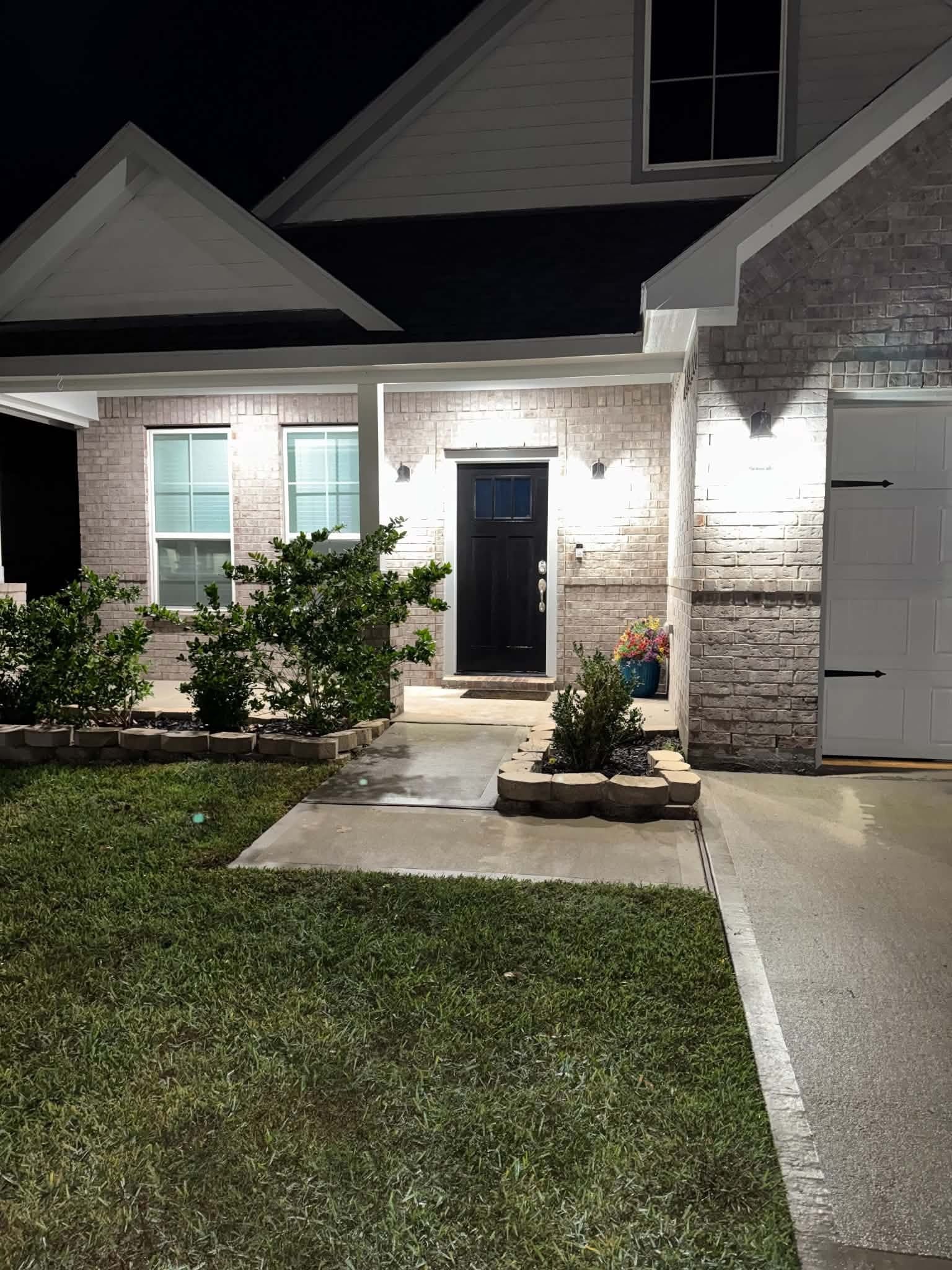 Charming home with a welcoming front porch, elegant black door, and beautifully lit exterior. The landscaped pathway leads to a well-maintained lawn, enhancing curb appeal.
