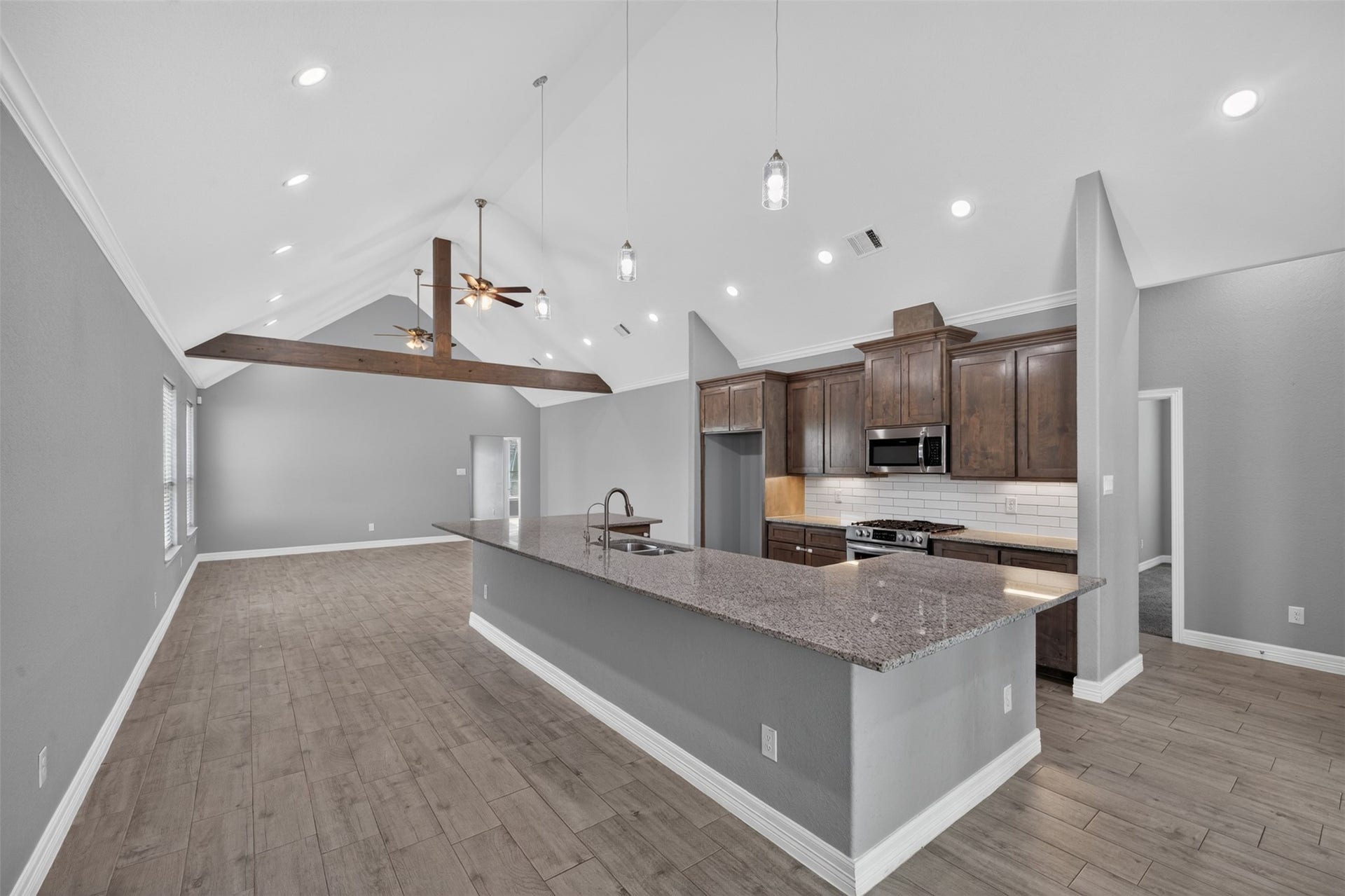 Spacious open-concept kitchen and living area featuring high vaulted ceilings with exposed wooden beams, modern fixtures, and elegant dark wood cabinetry.