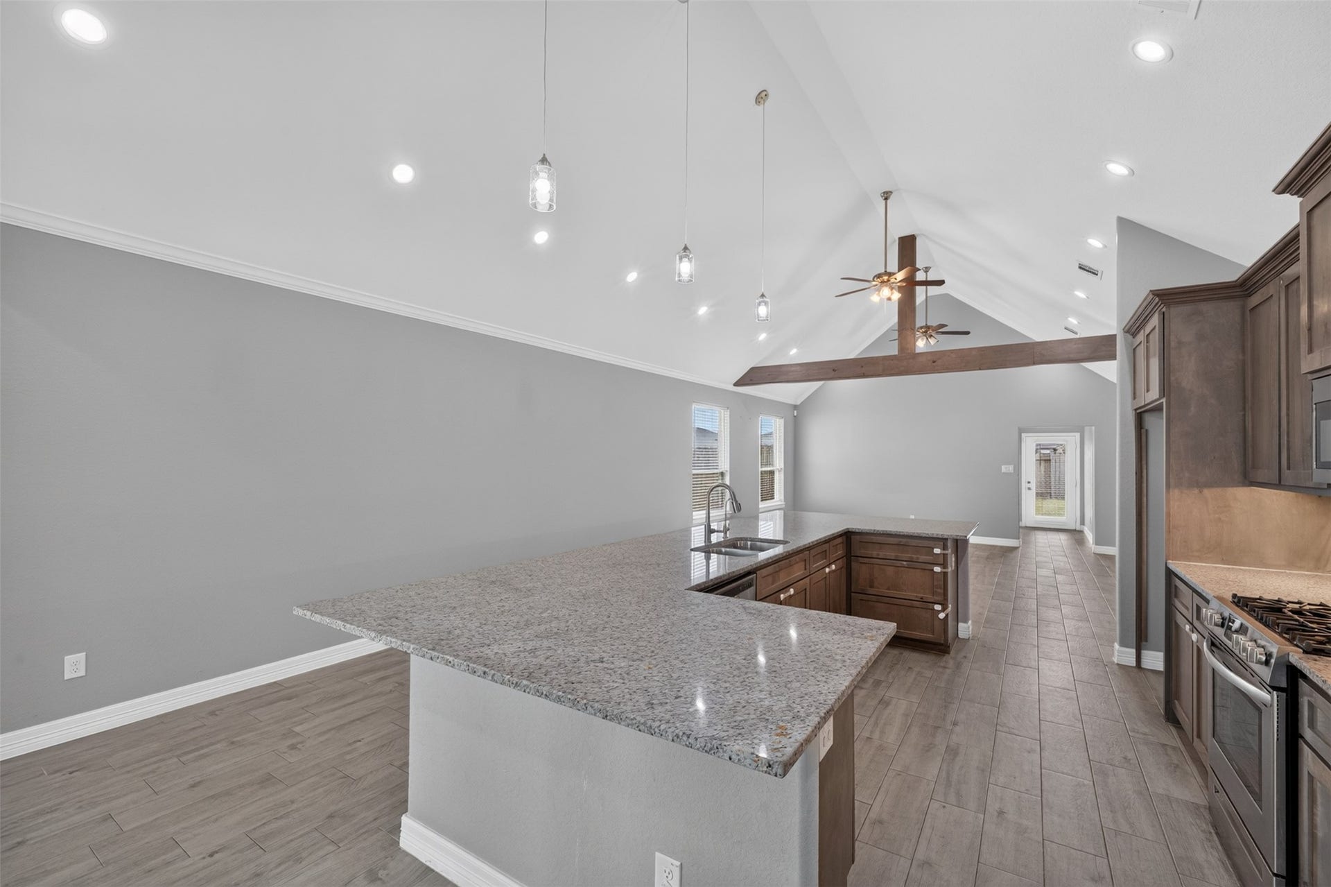 Spacious kitchen featuring high vaulted ceilings, modern pendant lighting, and a large granite island with ample seating. Stunning wood cabinetry complements the stainless steel appliances, while the open layout leads seamlessly into a bright living area.