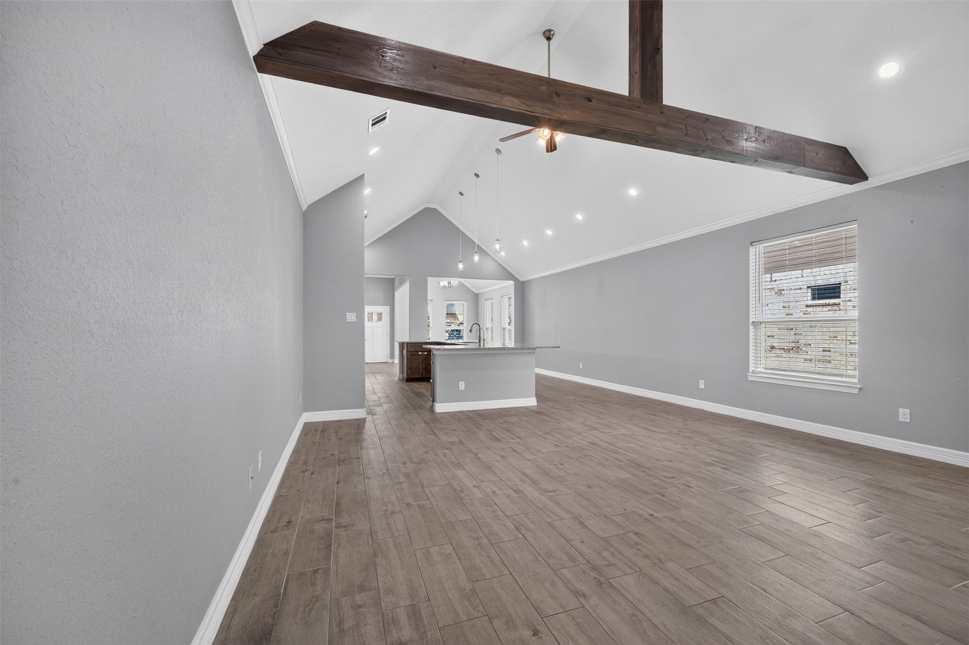 Spacious open-concept living area with vaulted ceilings, exposed wood beams, and elegant wood-look flooring, leading to a modern kitchen with a large island.