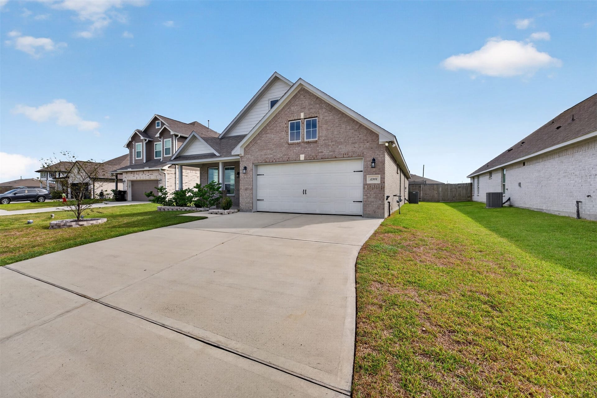 Charming brick home featuring a spacious driveway, lush green lawn, and a two-car garage, nestled in a friendly neighborhood.