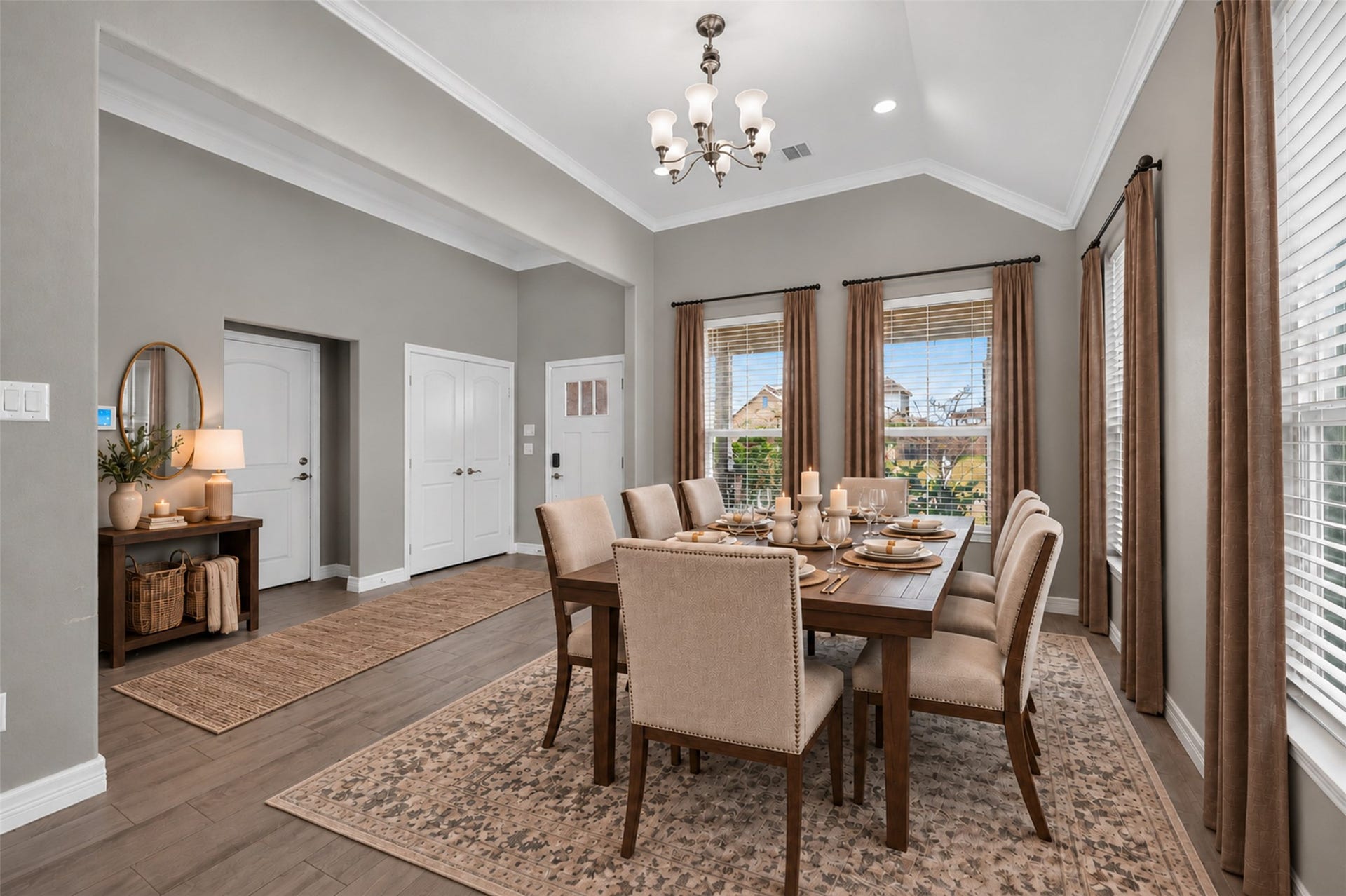 Elegant dining room with high ceilings, featuring a large wooden table and upholstered chairs. Natural light streams through the windows, highlighting the warm, neutral decor and stylish chandelier.