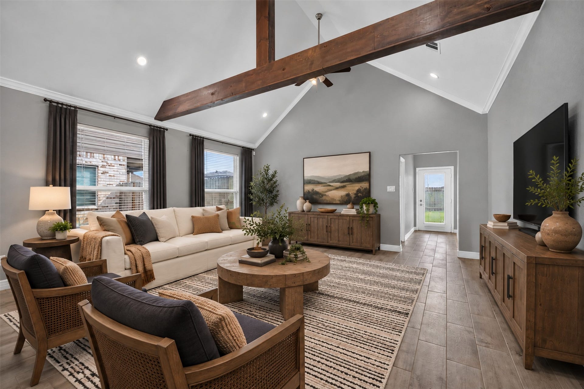 Spacious living room with vaulted ceilings and exposed wooden beam, featuring elegant wood flooring and abundant natural light. Cozy seating arrangement complements the stylish decor, creating an inviting atmosphere.