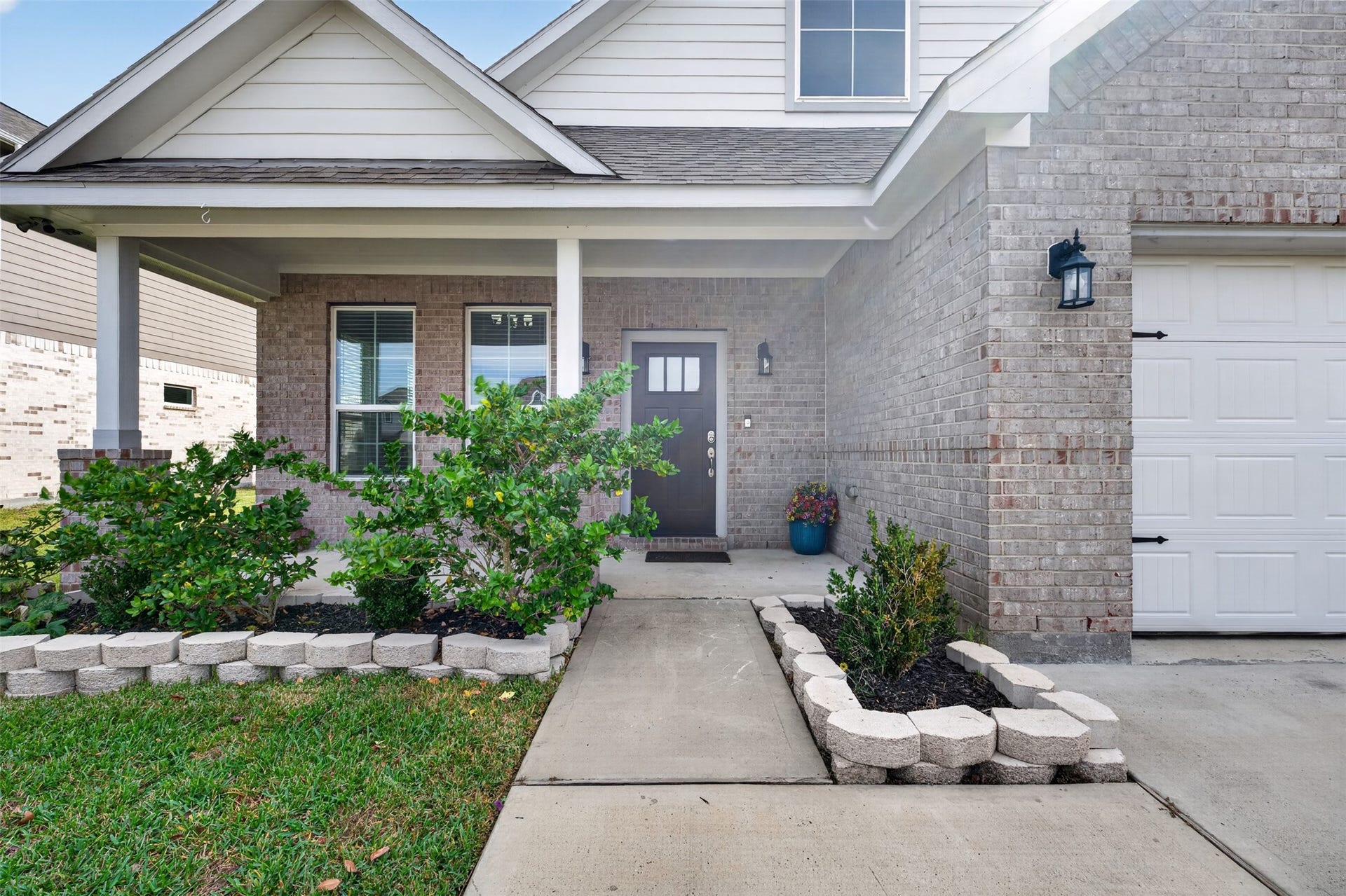 Charming brick home with a welcoming front porch, landscaped garden beds, and a stylish entryway.