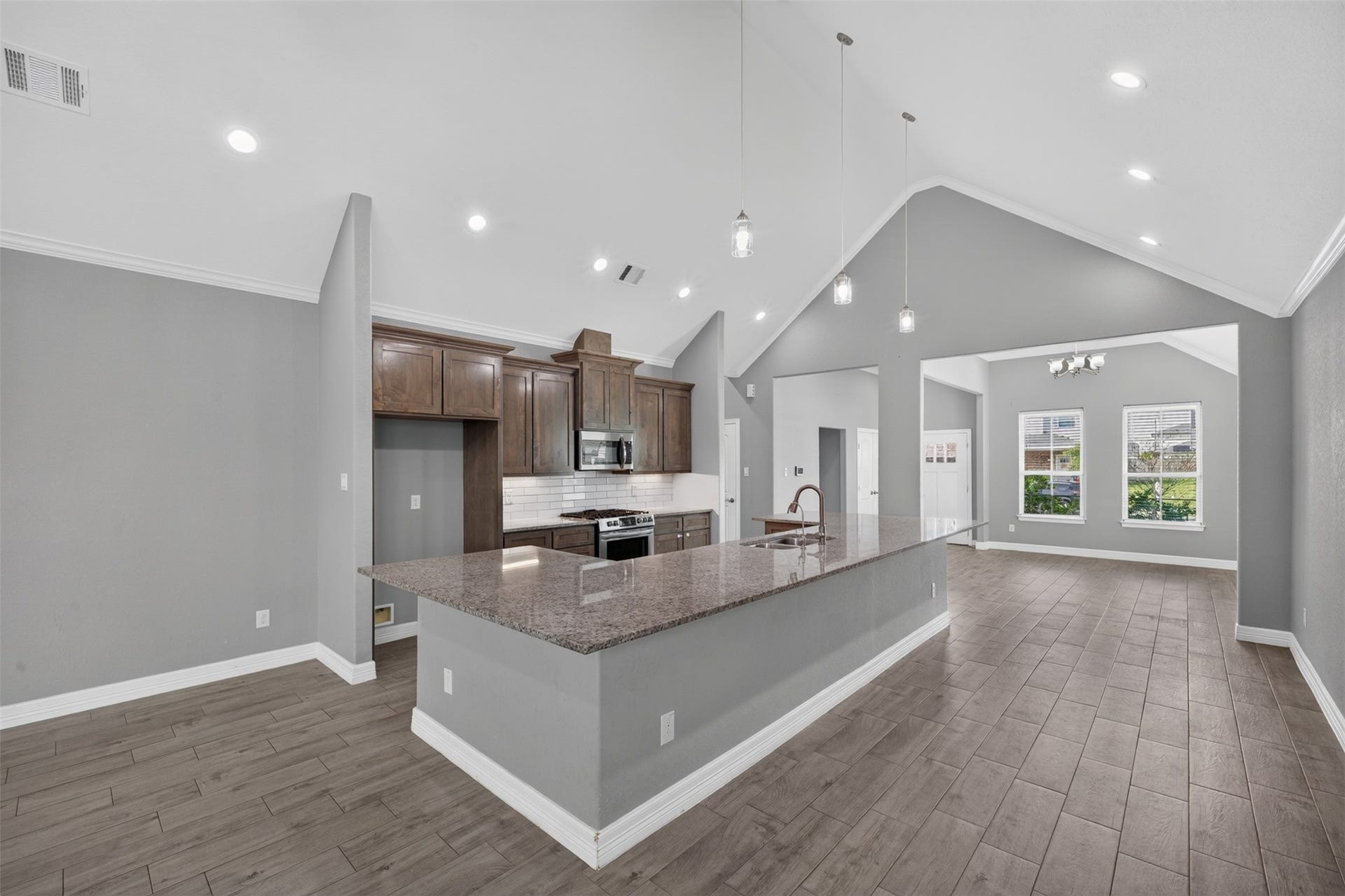 Spacious open-concept kitchen and living area featuring high vaulted ceilings, modern lighting, and a large granite island with ample seating.