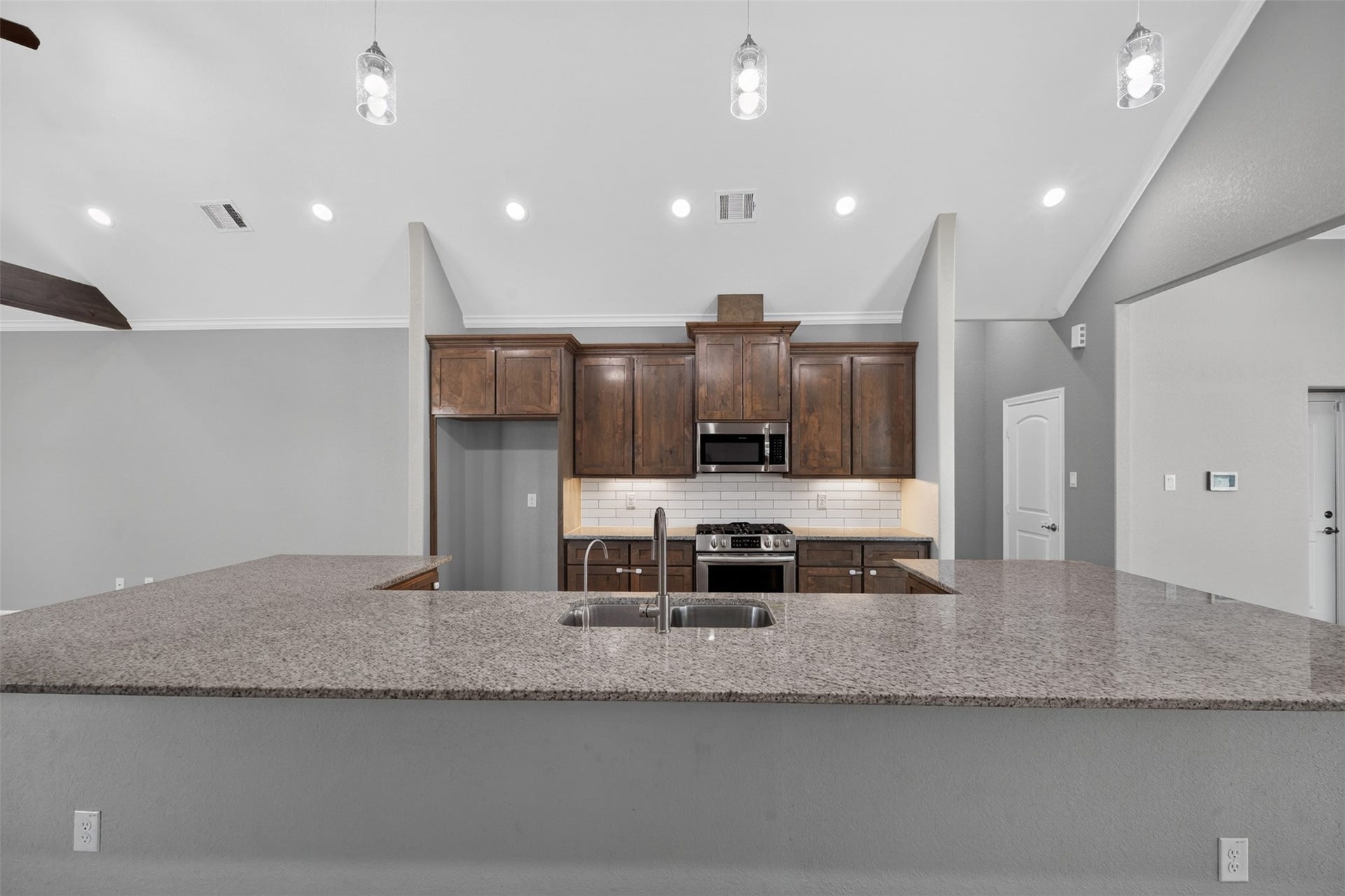 Spacious kitchen with sleek granite countertops, modern stainless steel appliances, and elegant pendant lighting, perfect for culinary enthusiasts.