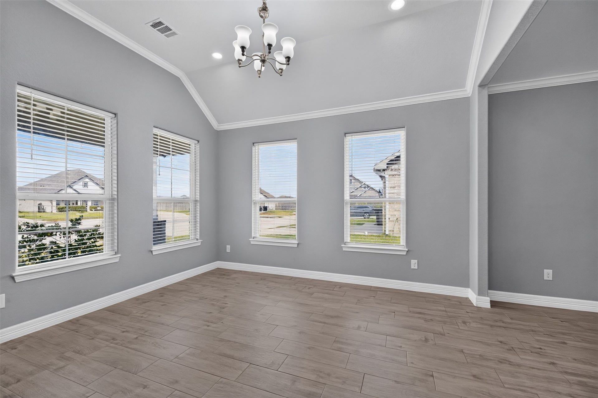 Bright and airy room with large windows, elegant light fixture, and stylish wood-look flooring, perfect for a dining area or living space.