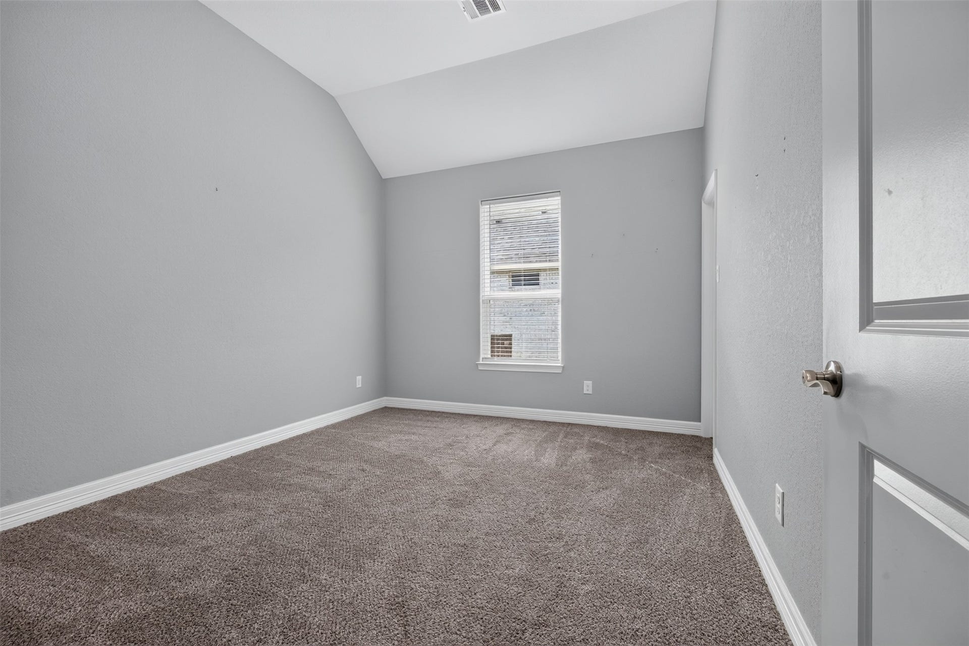 Cozy bedroom with soft carpeting, a neutral gray color palette, and a vaulted ceiling, offering a tranquil retreat.