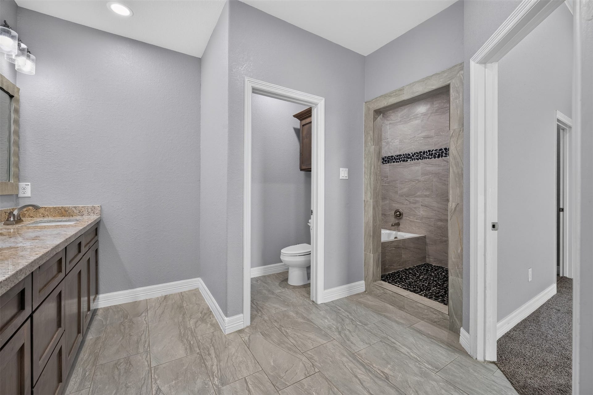 Spacious bathroom featuring elegant tile flooring, a dual-sink vanity with granite countertops, and a modern walk-in shower with stylish tile accents.