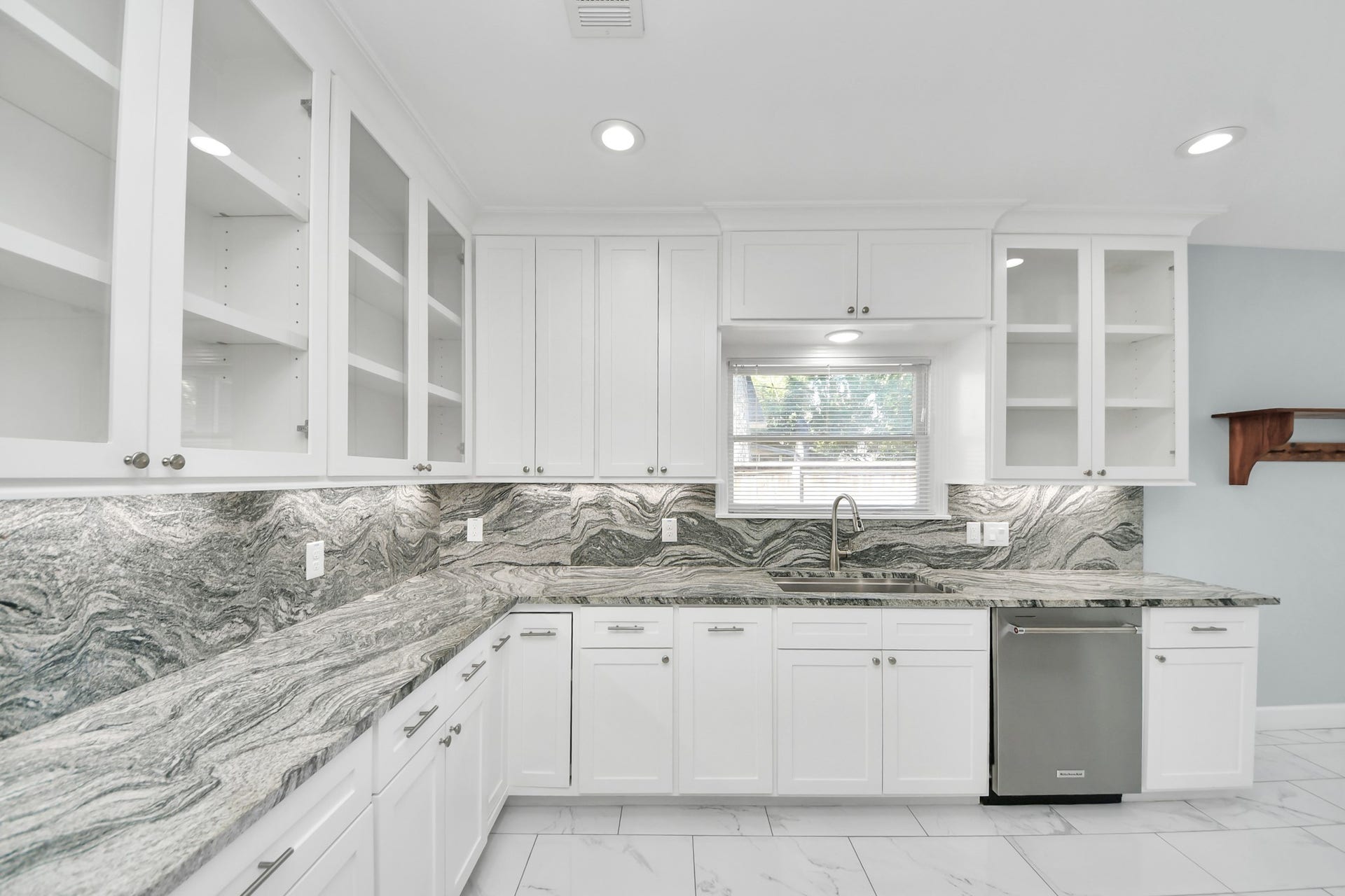 909 Fugate Street, Houston, TX 77009 Elegant kitchen featuring white cabinetry with glass-front doors, striking marble countertops, and modern stainless steel appliances.