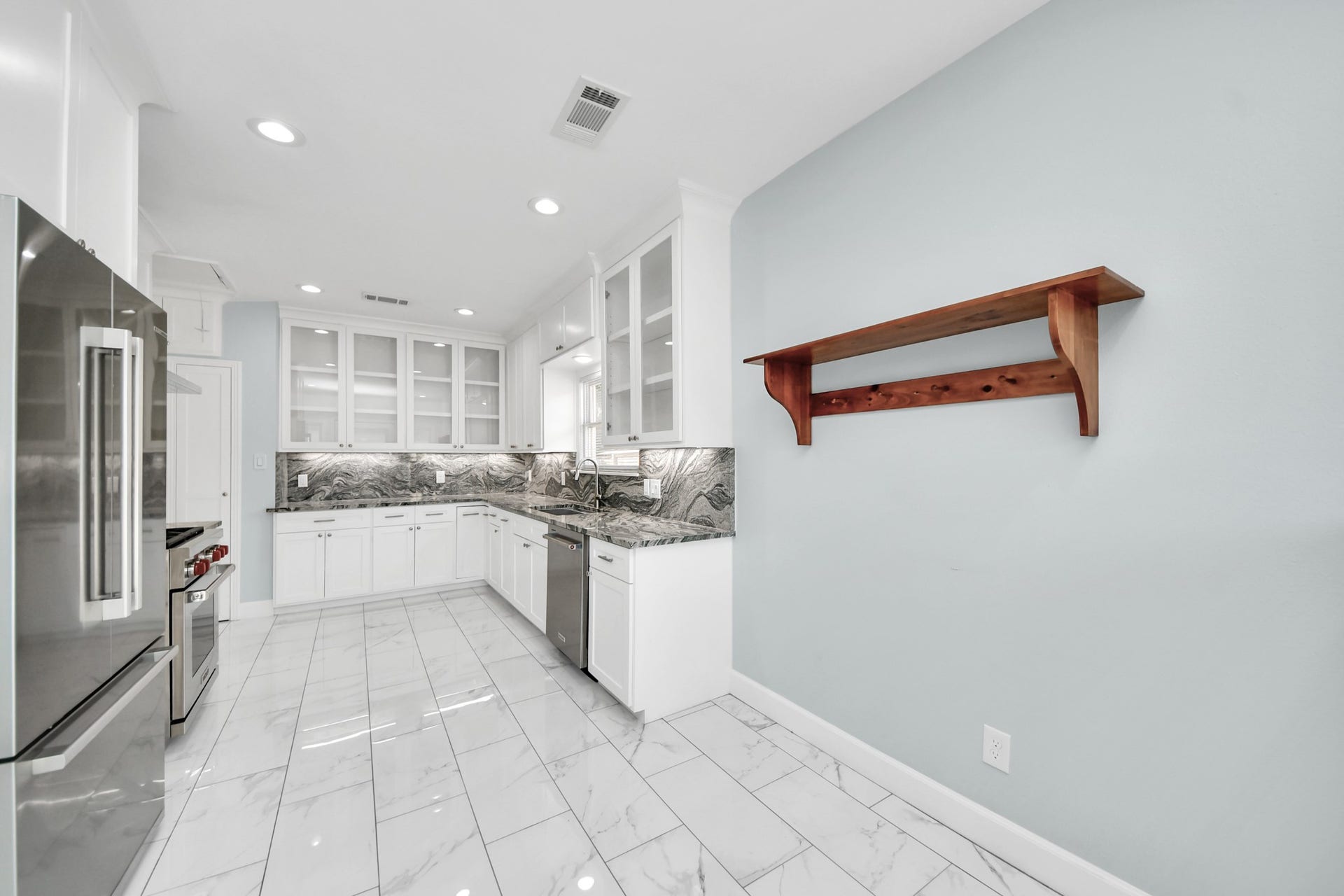 909 Fugate Street, Houston, TX 77009 Bright and modern kitchen featuring sleek stainless steel appliances, elegant white cabinetry with glass doors, and a striking marble backsplash, complemented by glossy tiled floors and a custom wooden shelf.