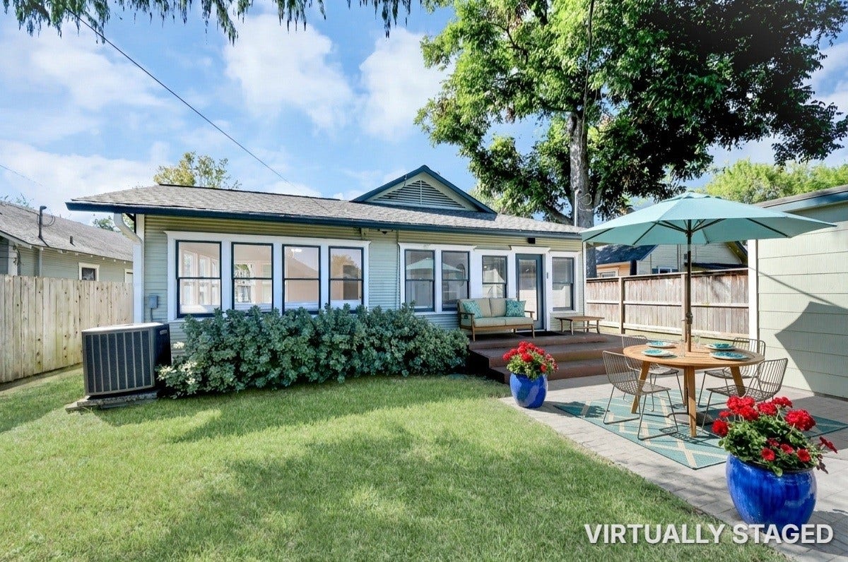 909 Fugate Street, Houston, TX 77009 Charming backyard oasis featuring a spacious deck with cozy seating and a dining area under a large umbrella, surrounded by lush greenery and vibrant flowers.