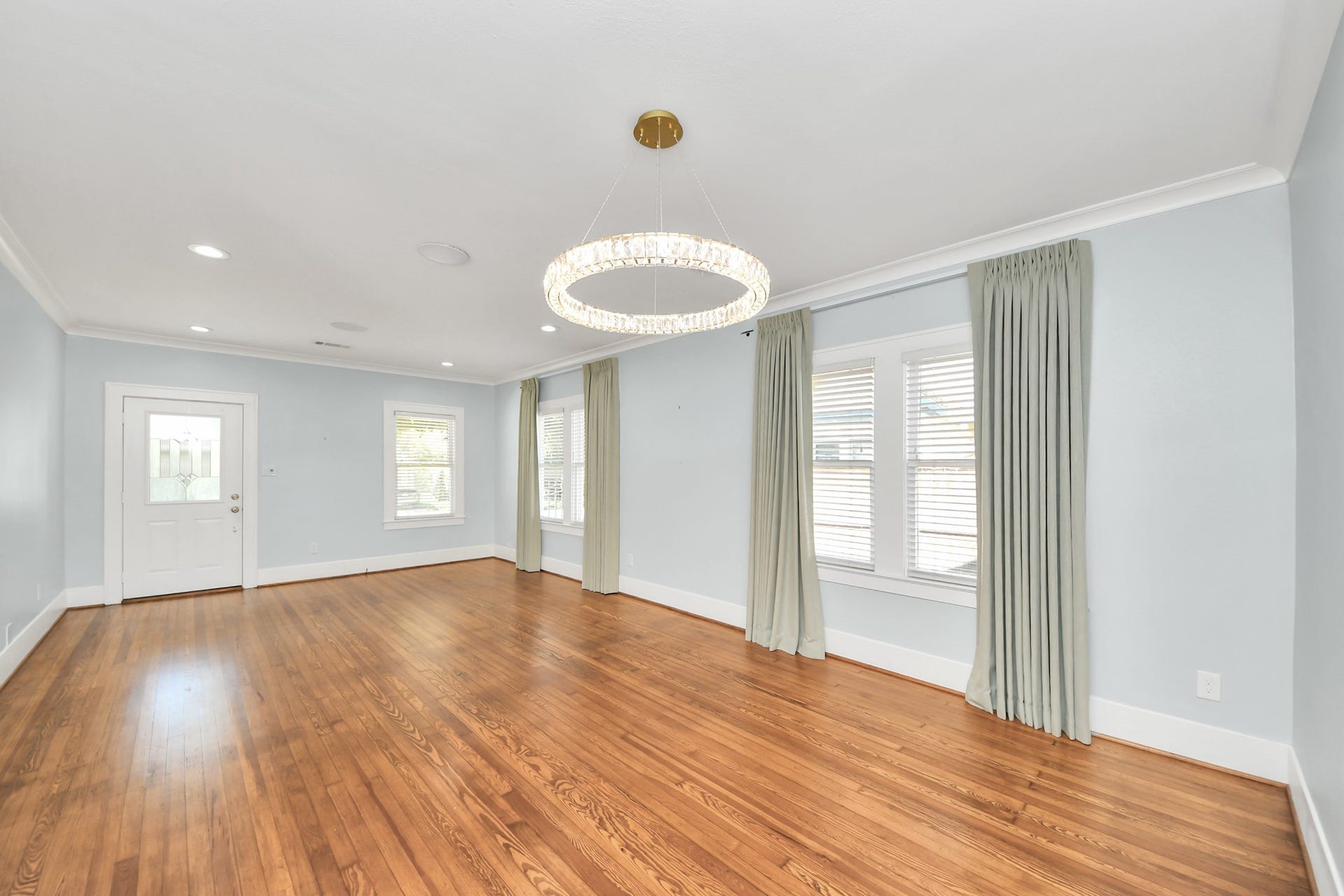 909 Fugate Street, Houston, TX 77009 Spacious living area with gleaming hardwood floors, large windows dressed in elegant drapes, and a modern chandelier adding a touch of sophistication.
