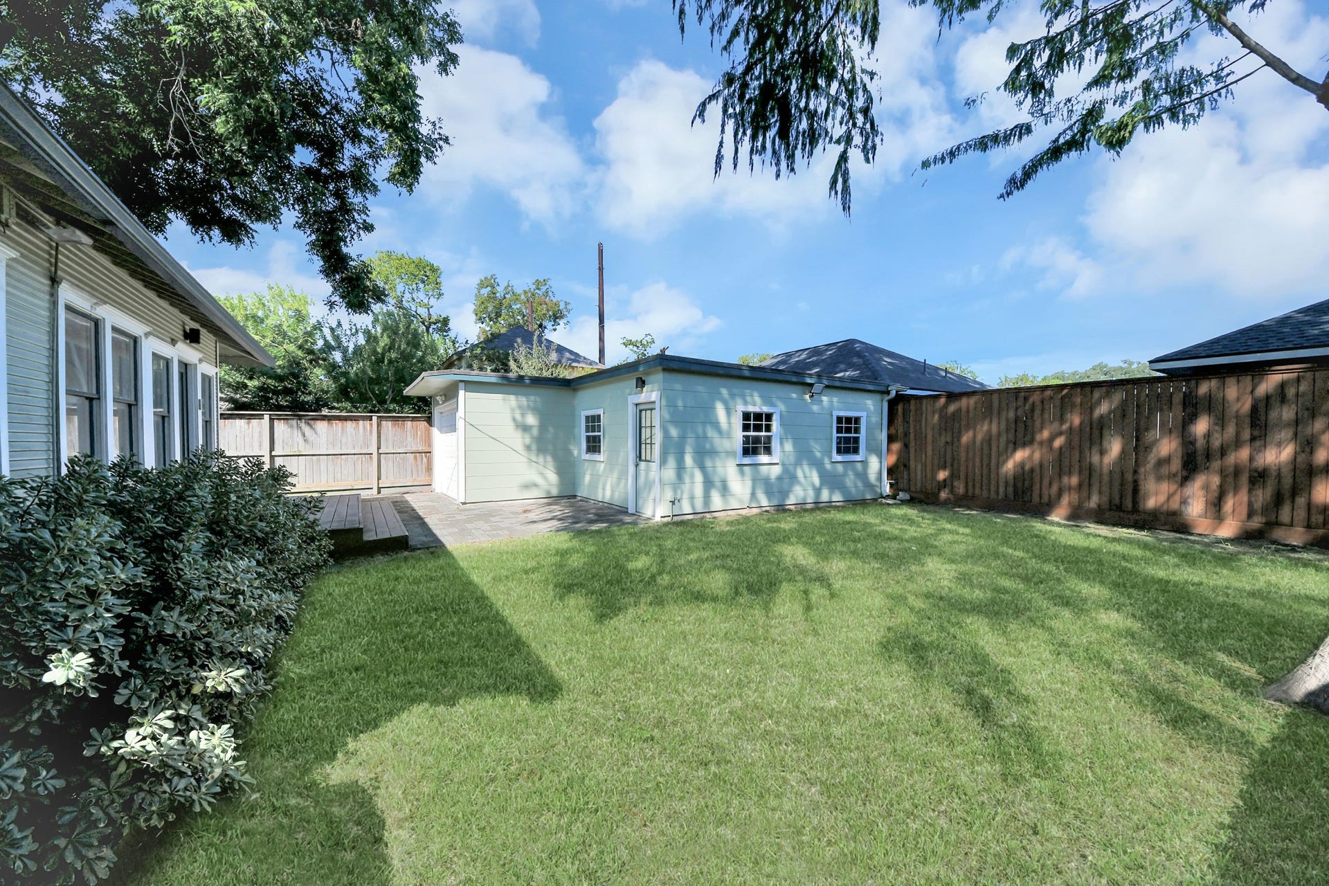 909 Fugate Street, Houston, TX 77009 Spacious backyard with lush green lawn, bordered by a wooden fence, and featuring a charming light blue outbuilding perfect for storage or a workshop.