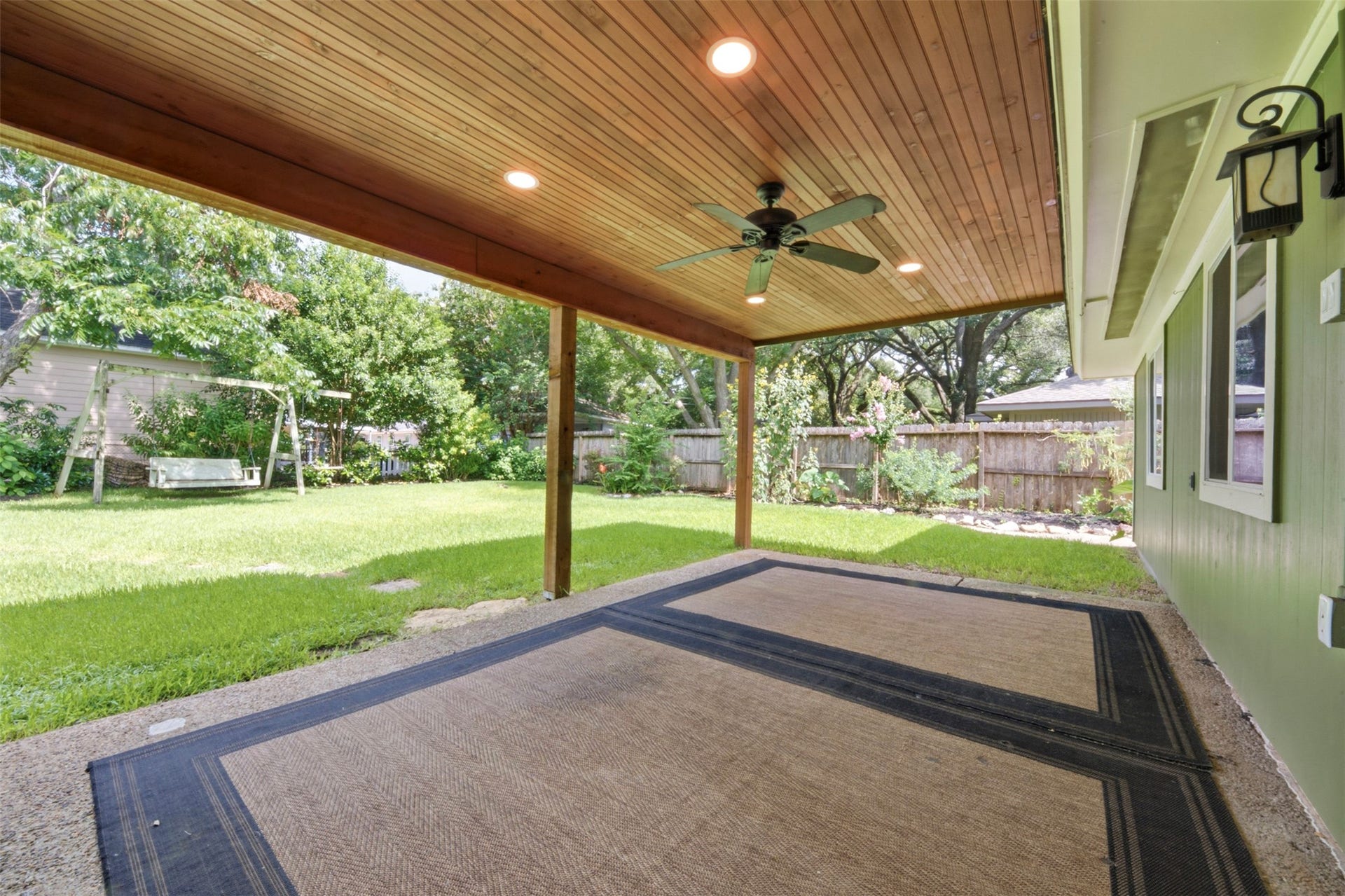 410 Kyle Street, Sugar Land, TX 77478 The expanded covered patio showcases a warm wood plank ceiling, recessed lighting, and a ceiling fan, creating a comfortable extension of the home's living space.