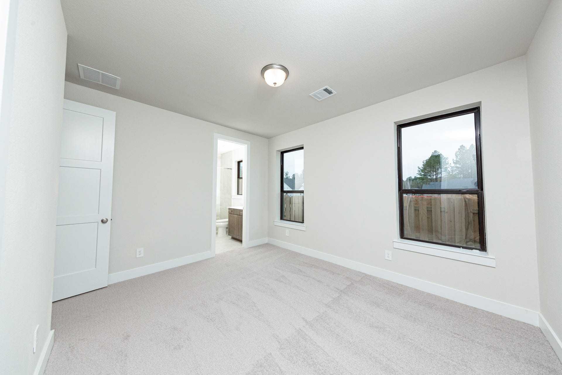 The ideal setup for multi-generational living or extended stays, this guest bedroom on the first floor includes its own dedicated en suite bath. It features high ceilings, large windows, plush carpet flooring, and neutral-toned walls.