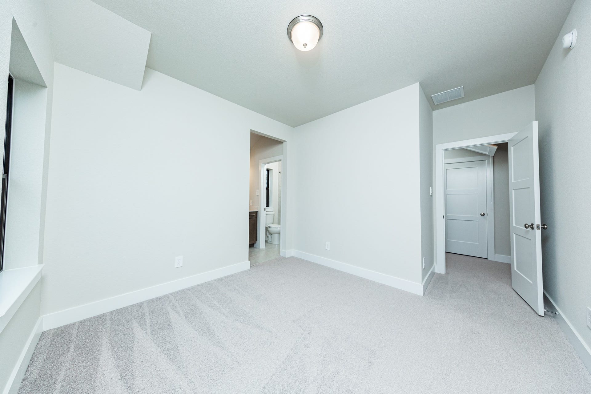 This inviting secondary bedroom combines comfort and modern elegance, featuring plush carpeting, a neutral color palette, and abundant natural light streaming through a large window. Discover the efficiency and convenience of accessing the secondary bathroom with another secondary bedroom--a highly functional solution for busy families.