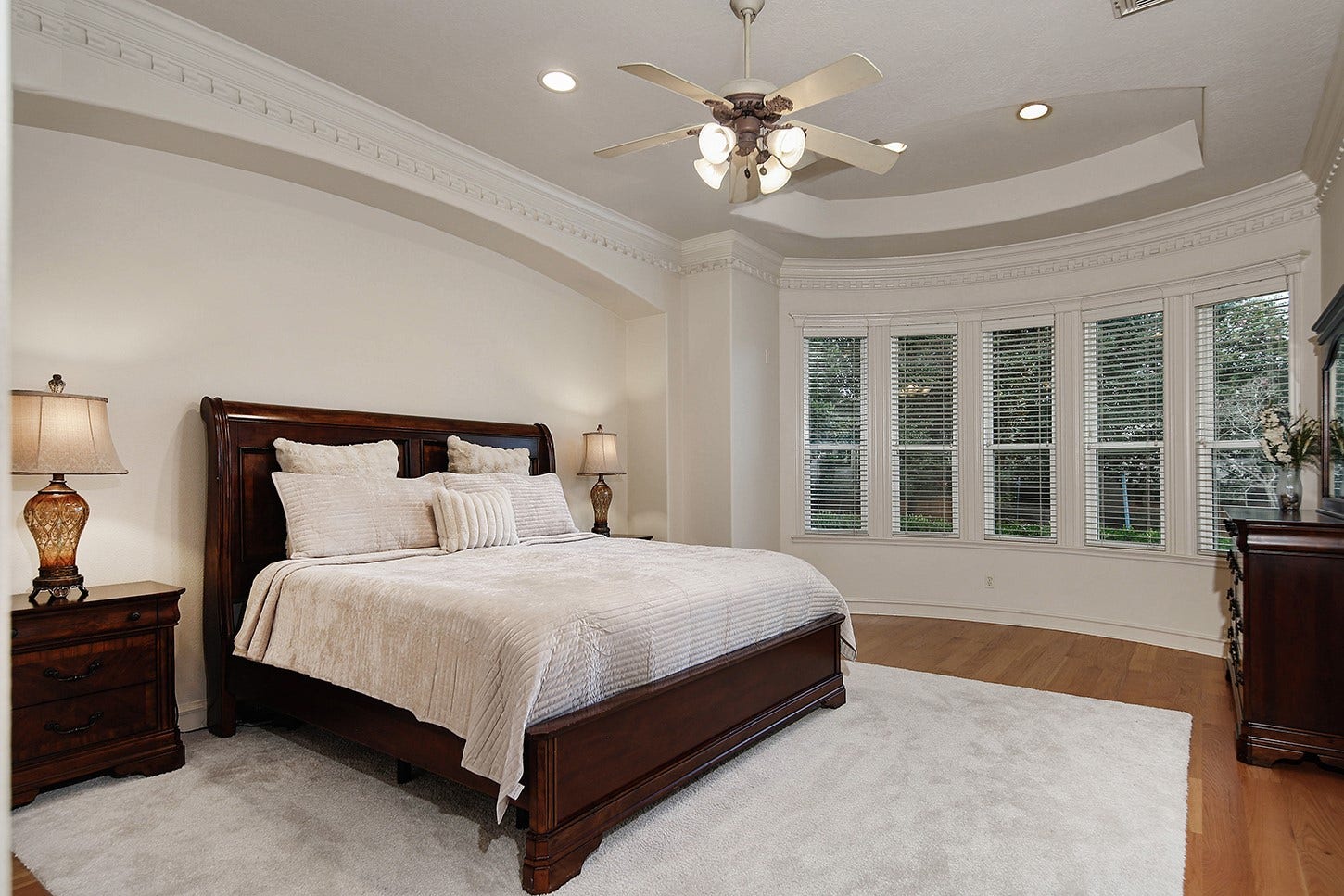 10 Snow Pond Place, The Woodlands, TX 77382 The spacious primary suite features a recessed headboard wall accented with elegant molding. Enhanced by warm wood flooring and designer white walls, the room offers a sophisticated, neutral aesthetic suitable for any decor style.
