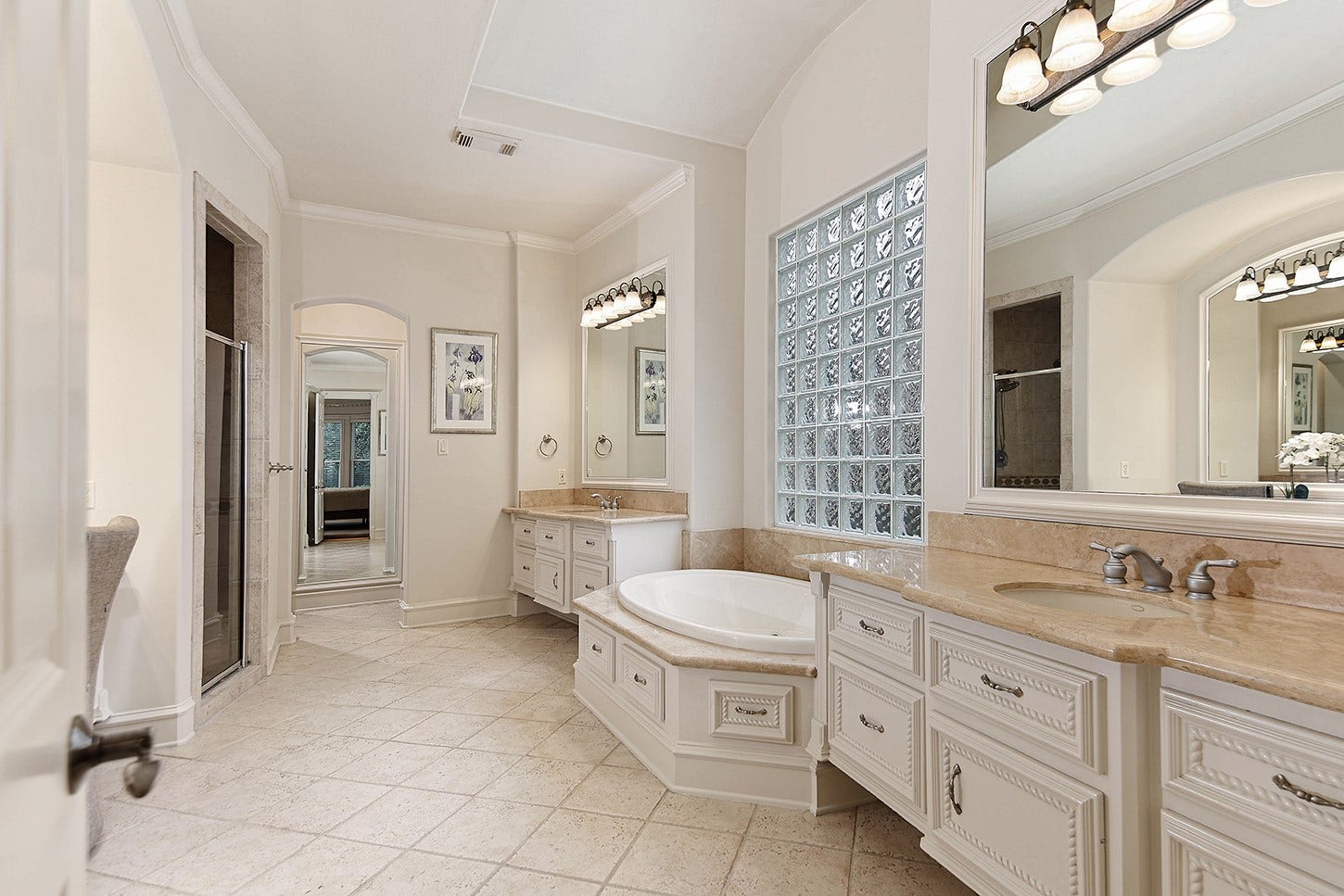 10 Snow Pond Place, The Woodlands, TX 77382 The primary ensuite features separate, custom-designed vanity areas with high-end cabinetry and marble countertops, positioned to frame a spacious garden soaking tub accented by a glass block window for natural lighting.