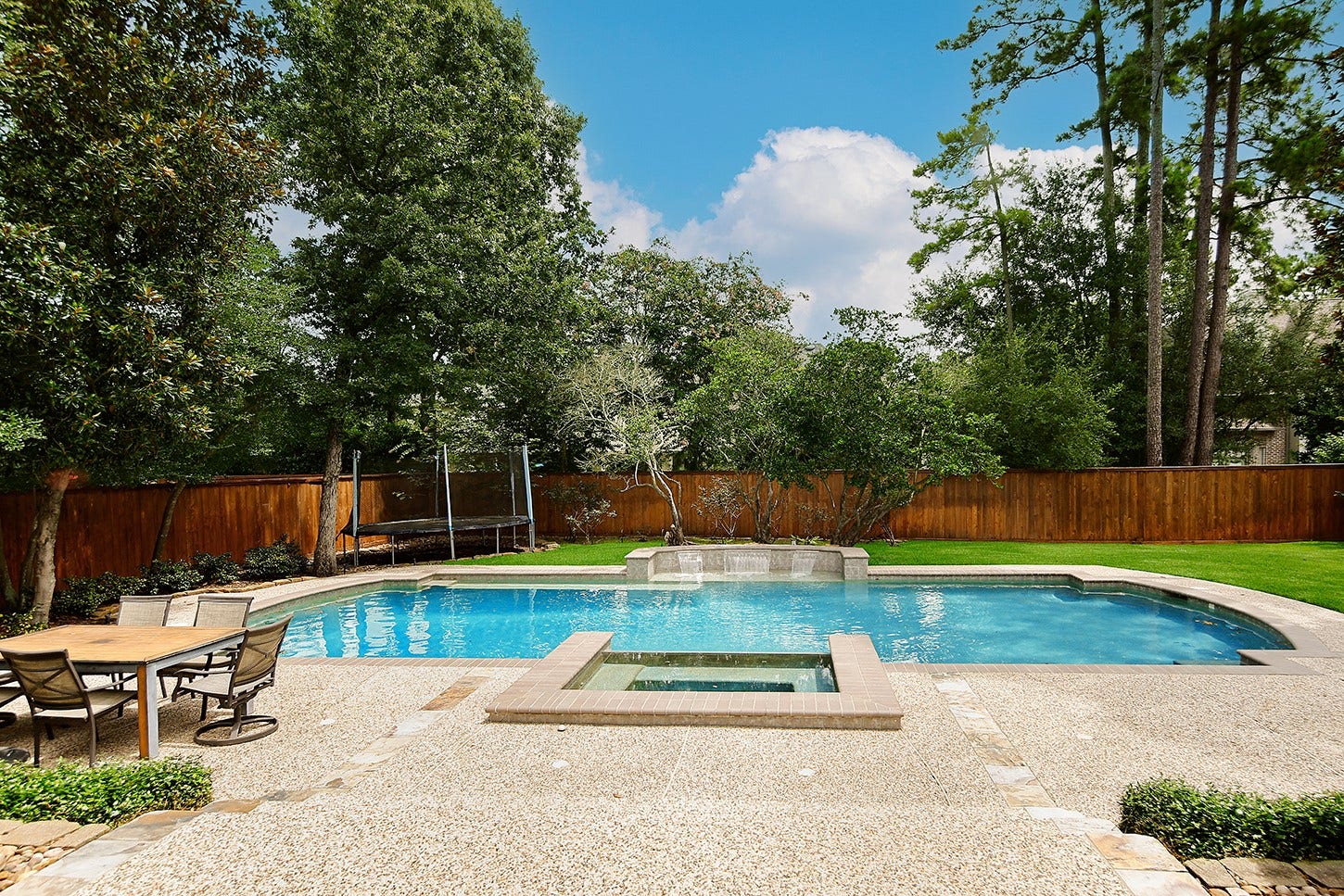 10 Snow Pond Place, The Woodlands, TX 77382 This private backyard features a sprawling pool and spa, offering a resort-style atmosphere complemented by lush lawn and landscaping.