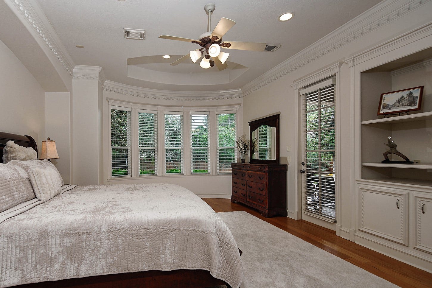 10 Snow Pond Place, The Woodlands, TX 77382 This primary suite is elevated by exceptional architectural features, including a curved window bay that creates an inviting sitting area with tranquil views of the backyard oasis. A convenient glass door allows easy access to lanai and pool. Custom recessed built-in shelves with cabinets are perfect for decor and storage.