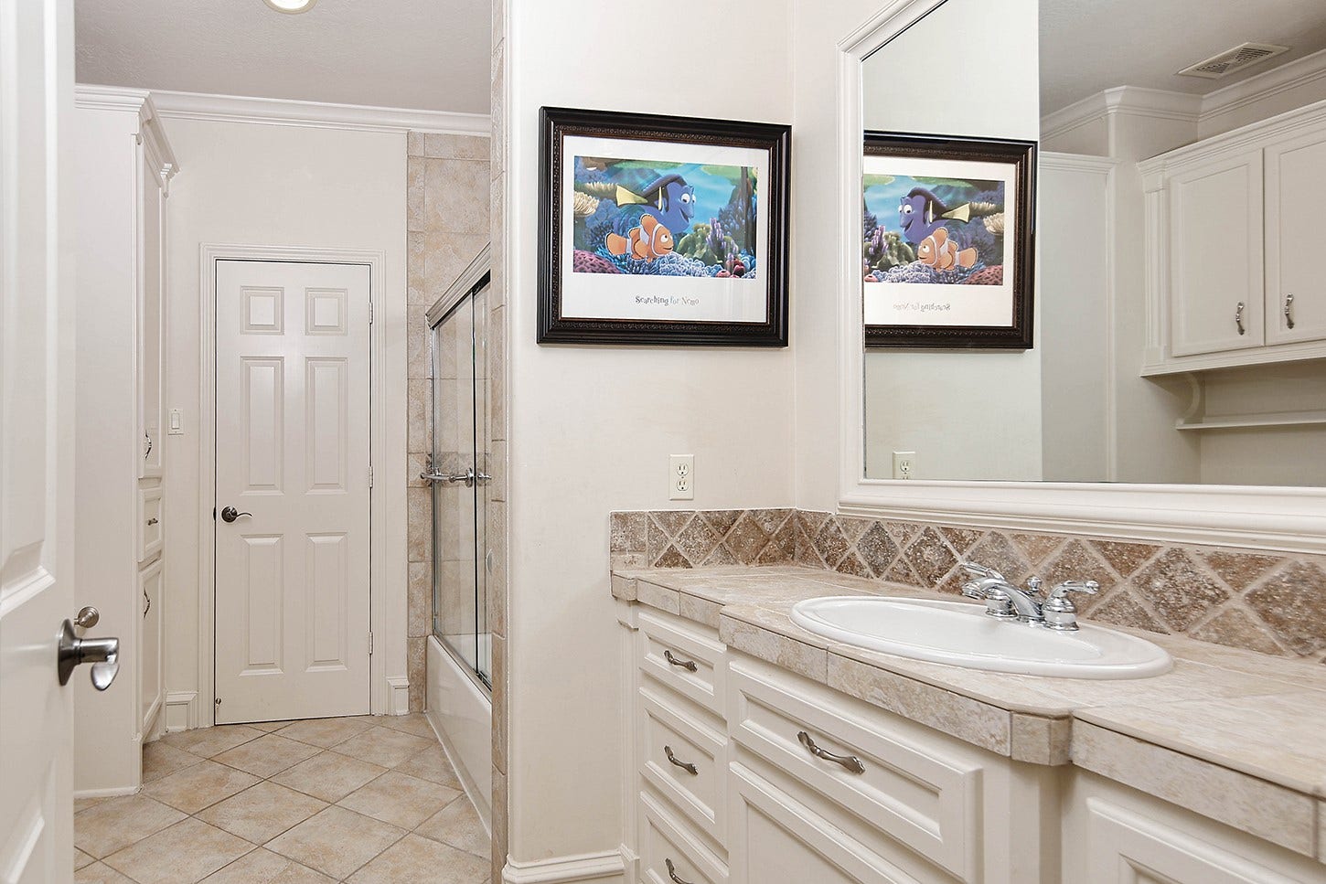 10 Snow Pond Place, The Woodlands, TX 77382 Bathroom 2 features ample counter space, custom cabinetry for storage, and an expansive mirror. The tub/shower combination is enclosed by a glass sliding door.