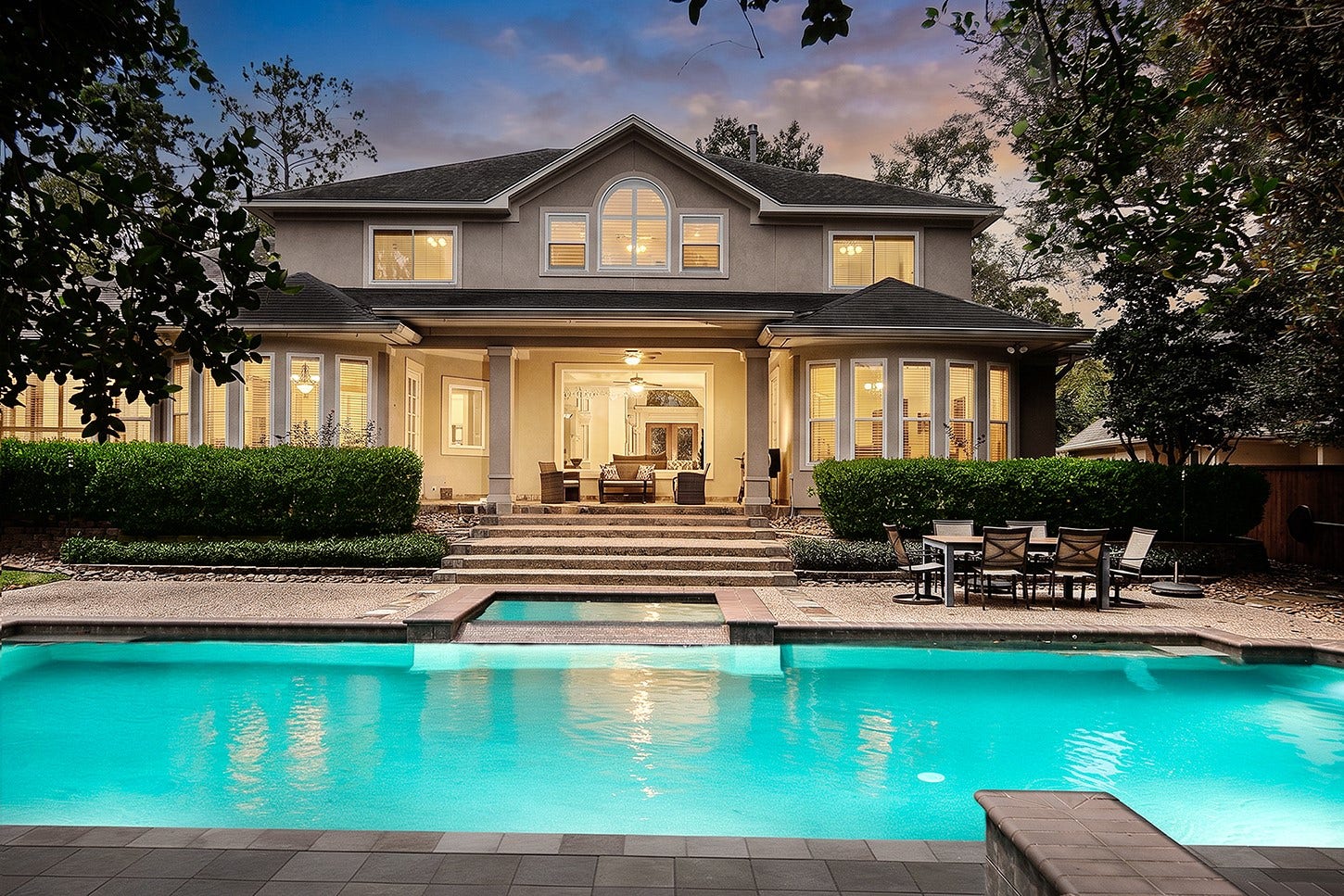 10 Snow Pond Place, The Woodlands, TX 77382 The backyard pool area is elegantly illuminated in the evening, with expansive windows providing a seamless transition between the indoor and outdoor living spaces. Meticulously manicured landscaping enhances the setting with vibrant colors, contributing to the sophisticated ambiance of the property.