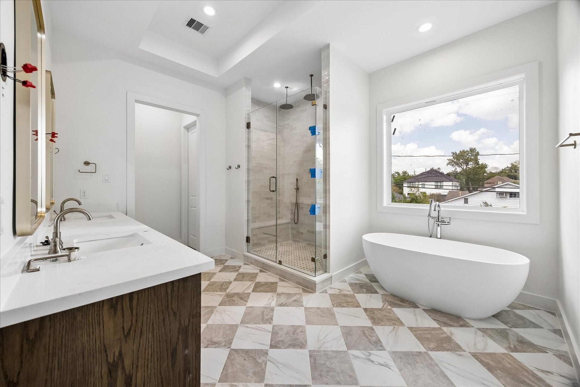1726 Chantilly Lane, Houston, TX 77018 A freestanding soaking tub and glass-enclosed shower anchor the primary bath. Checkerboard tile and warm metal fixtures bring contrast to the light finishes.