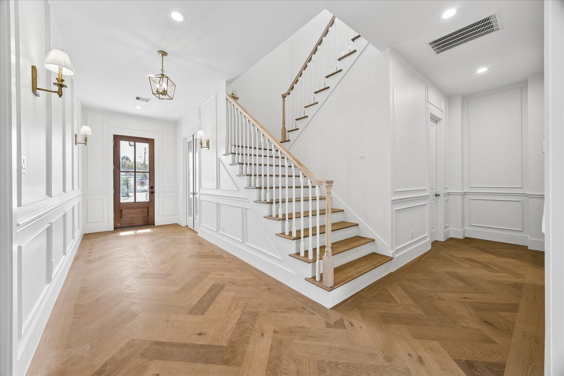 1726 Chantilly Lane, Houston, TX 77018 The entry connects to an open staircase with wood treads and a dark railing. Herringbone flooring and wall paneling carry the architectural detail through the front of the home.