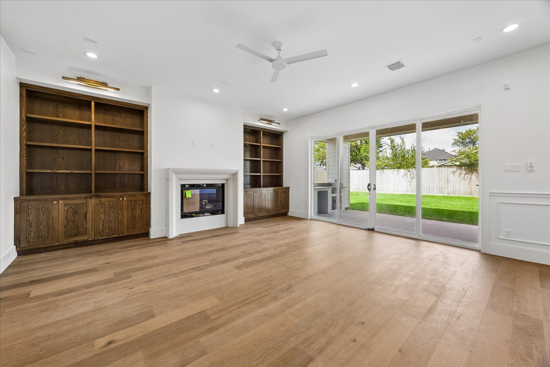 1726 Chantilly Lane, Houston, TX 77018 The living room centers on a cast-stone fireplace framed by wood built-ins. Sliding glass doors extend the view to the covered patio and fenced backyard, connecting the main gathering space with outdoor living.