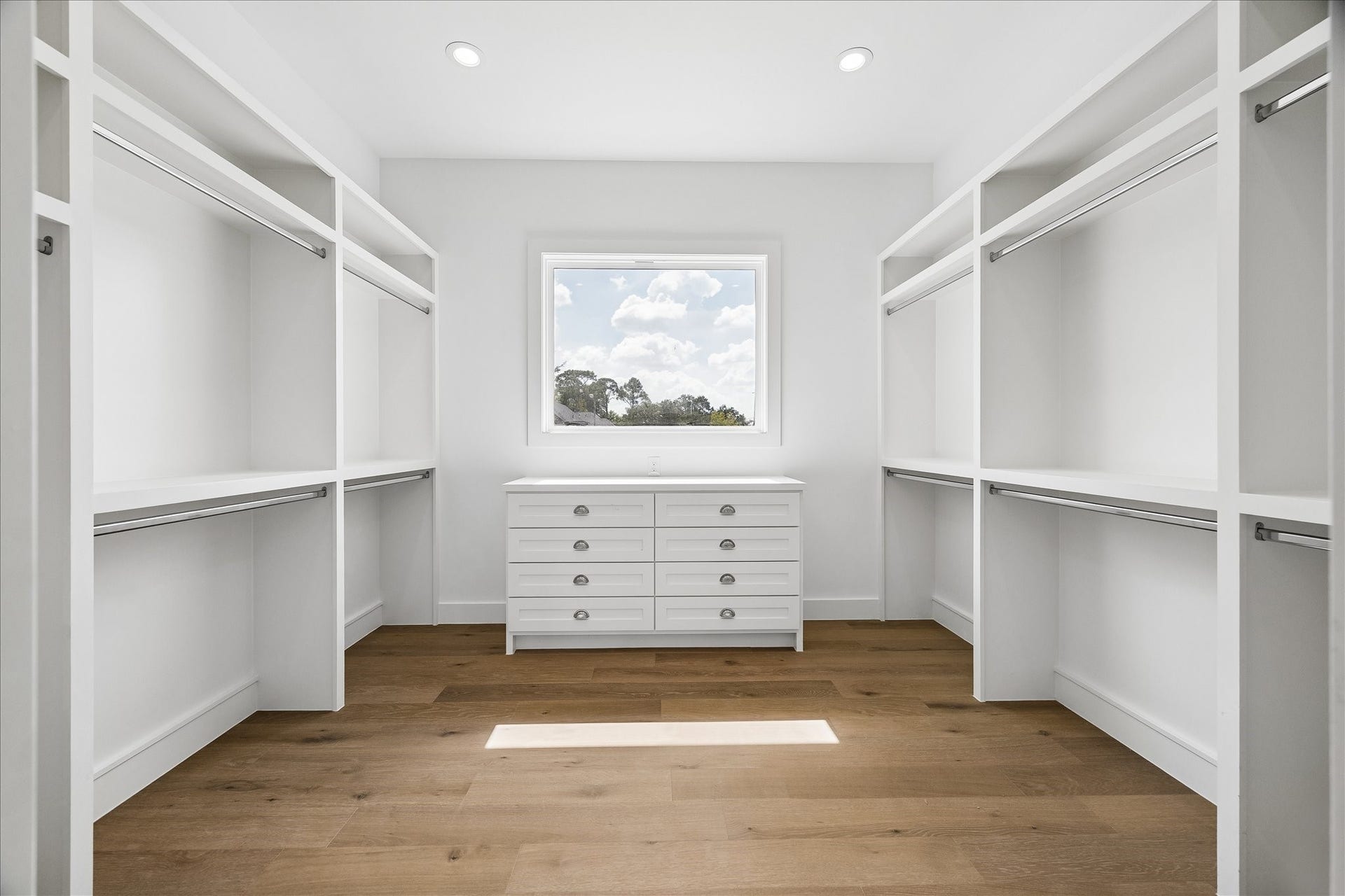 1726 Chantilly Lane, Houston, TX 77018 The primary walk-in closet combines hanging space, open shelving and built-in drawers. A window brings natural light to the dressing area, with wood flooring underfoot.