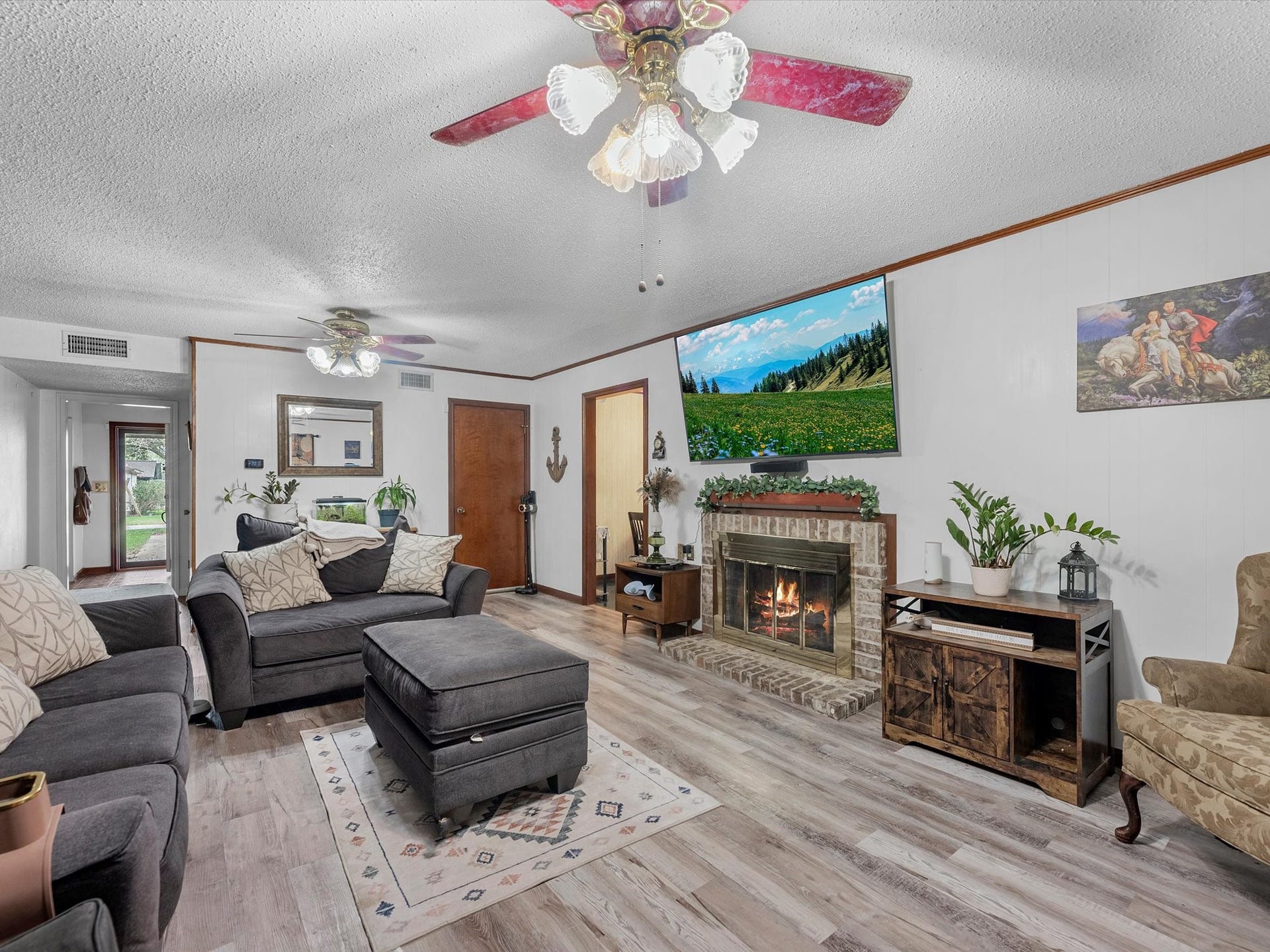 4101 Avenue O, Santa Fe, TX 77510 This cozy living room features light wood flooring and a neutral color palette, accented by eclectic decor and a detailed world map tapestry. It includes comfortable seating, ceiling fans, and opens to a bright adjoining room with garden views.