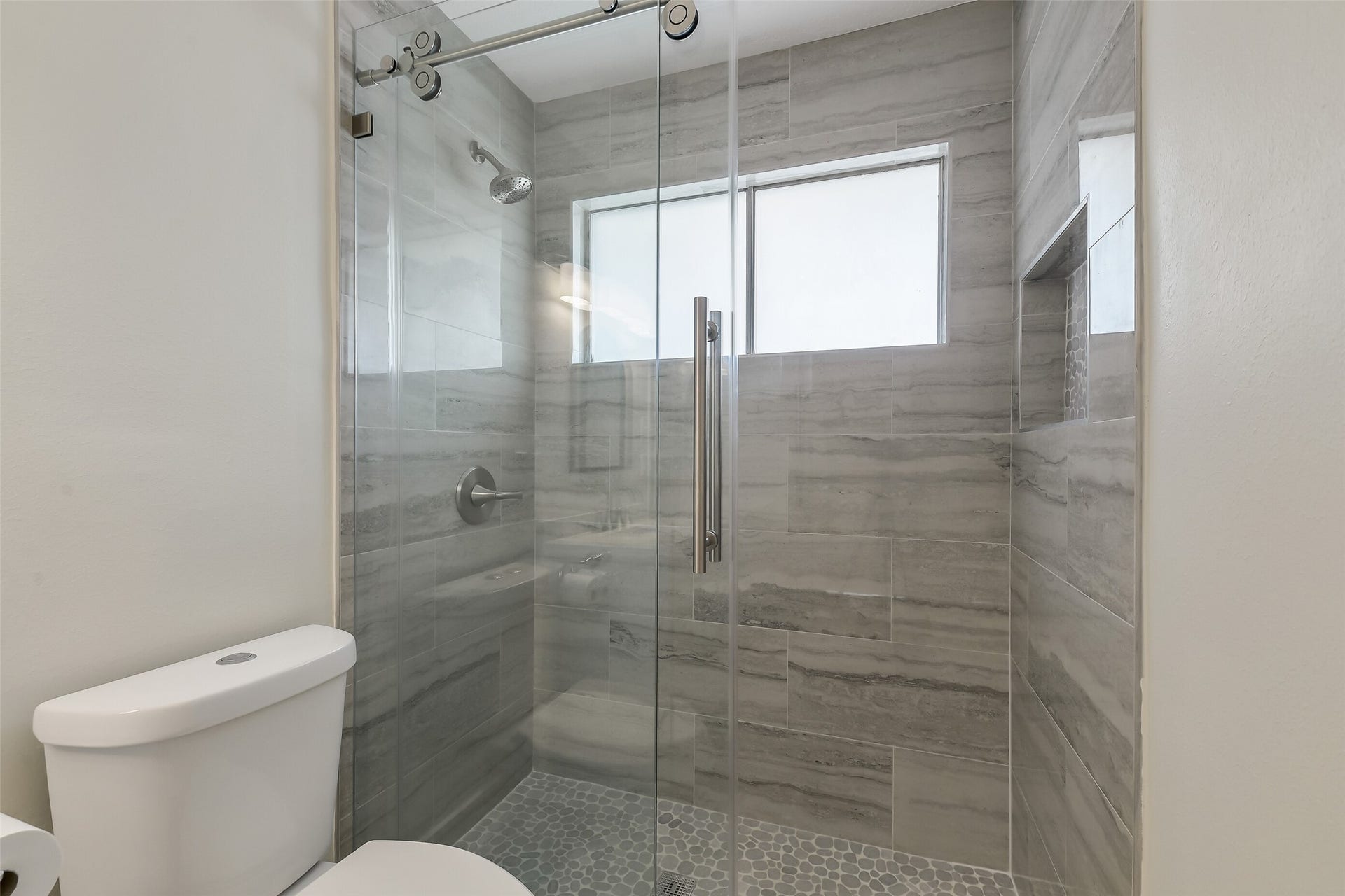 a fully remodeled walk-in shower with floor-to-ceiling tile, frameless glass and built-in niches