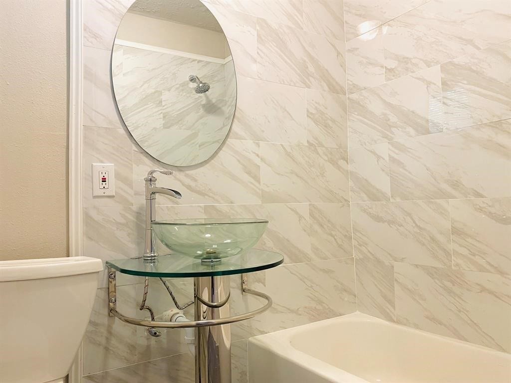 3406 Daphne St Street, #5, Houston, TX 77021 Chic bathroom featuring elegant marble-patterned tiles, a modern glass vessel sink, and a sleek round mirror for a luxurious touch.