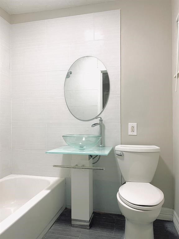 3406 Daphne St Street, #5, Houston, TX 77021 Modern bathroom featuring a sleek glass vessel sink, oval mirror, and elegant gray tiling, creating a clean and contemporary space.