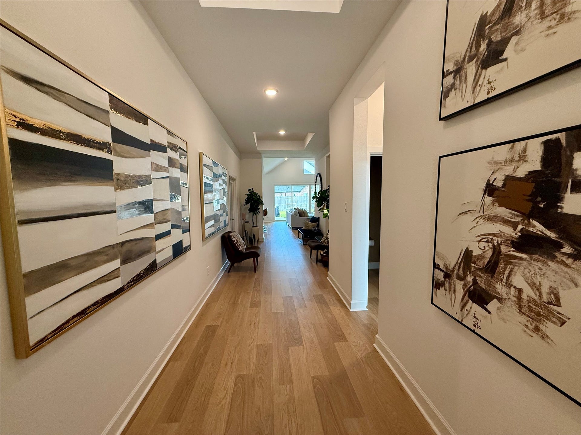 9911 Deep Water Drive, Missouri City, TX 77459 A welcoming hallway with elegant wooden flooring and modern abstract art leads to a bright, open living space, creating a stylish and inviting entrance.