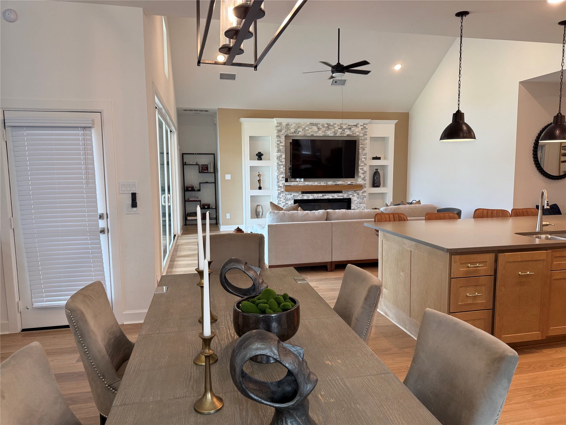 9911 Deep Water Drive, Missouri City, TX 77459 Spacious open-concept living area featuring a modern kitchen with pendant lighting, a cozy seating area, and a stylish custom designed stone fireplace with built-in shelving and a mounted TV.