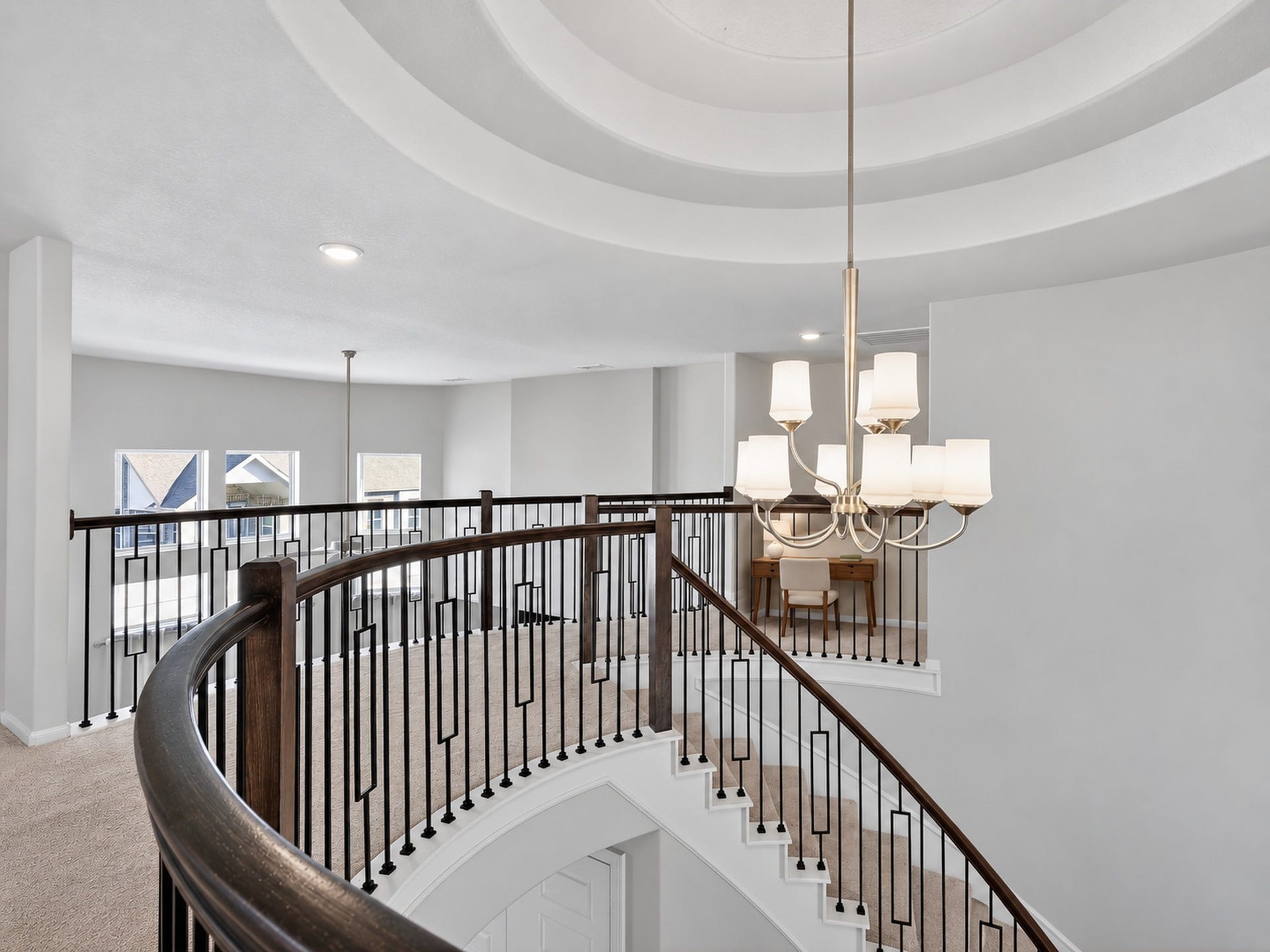 6714 Wellbrook Falls Lane, Katy, TX 77493 Curved staircase features dark metal balusters beneath a chandelier and tiered ceiling. (virtually staged)