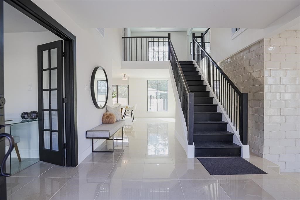 5614 Indian Circle, Houston, TX 77056 Grand entryway featuring striking tile flooring and a dramatic black wooden staircase that anchors the space with timeless elegance. Soaring ceilings and abundant natural light enhance the luxurious feel of this sophisticated welcome into the home.