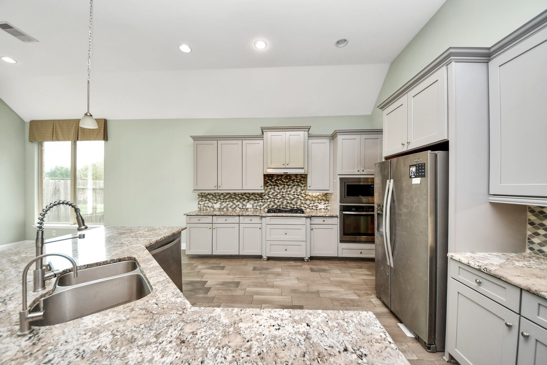 Well-appointed kitchen with extensive cabinetry, granite countertops, mosaic tile backsplash, stainless steel appliances, and generous workspace.