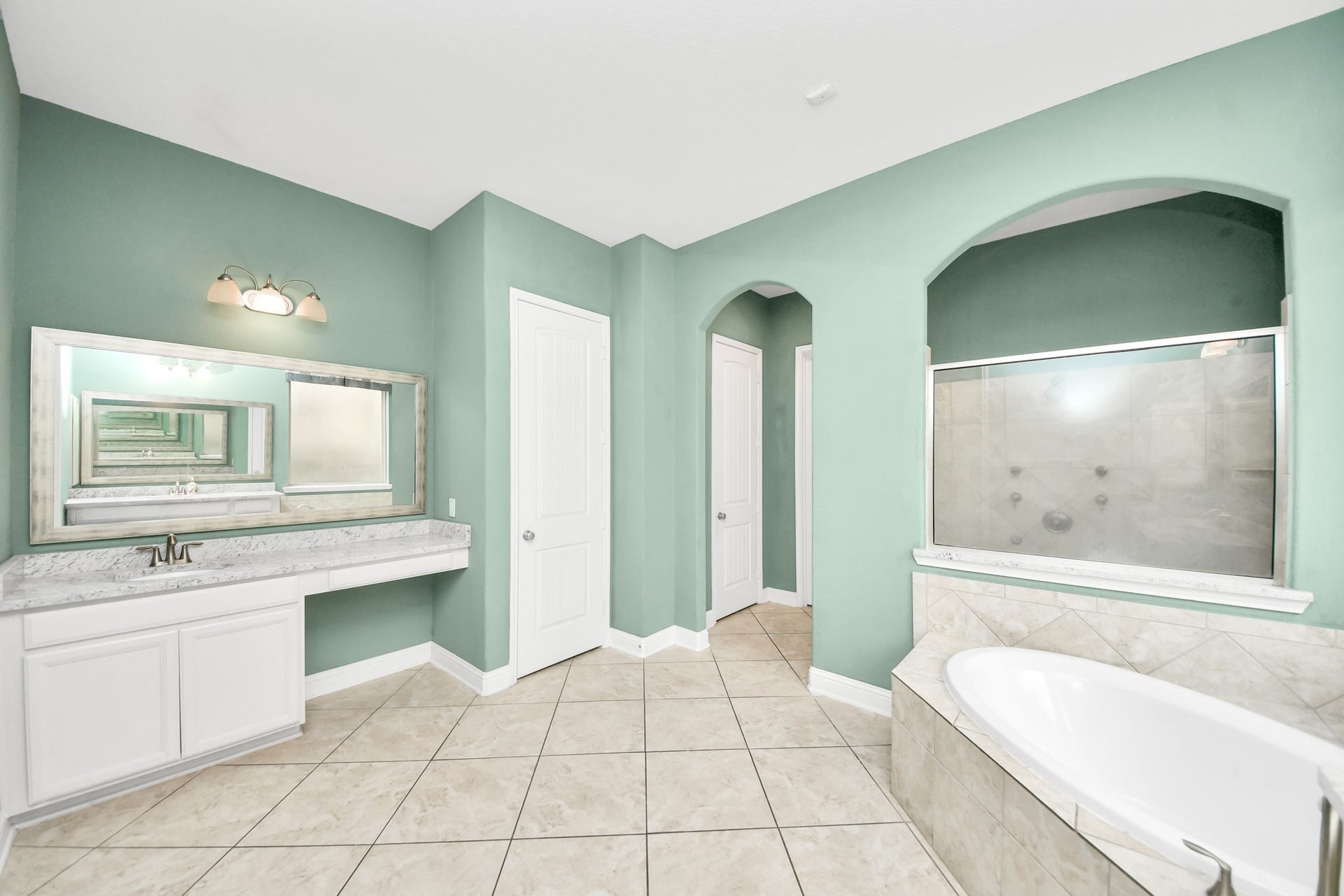 Relaxing primary bath with a tiled soaking tub, expansive vanity, oversized mirror, and separate shower.