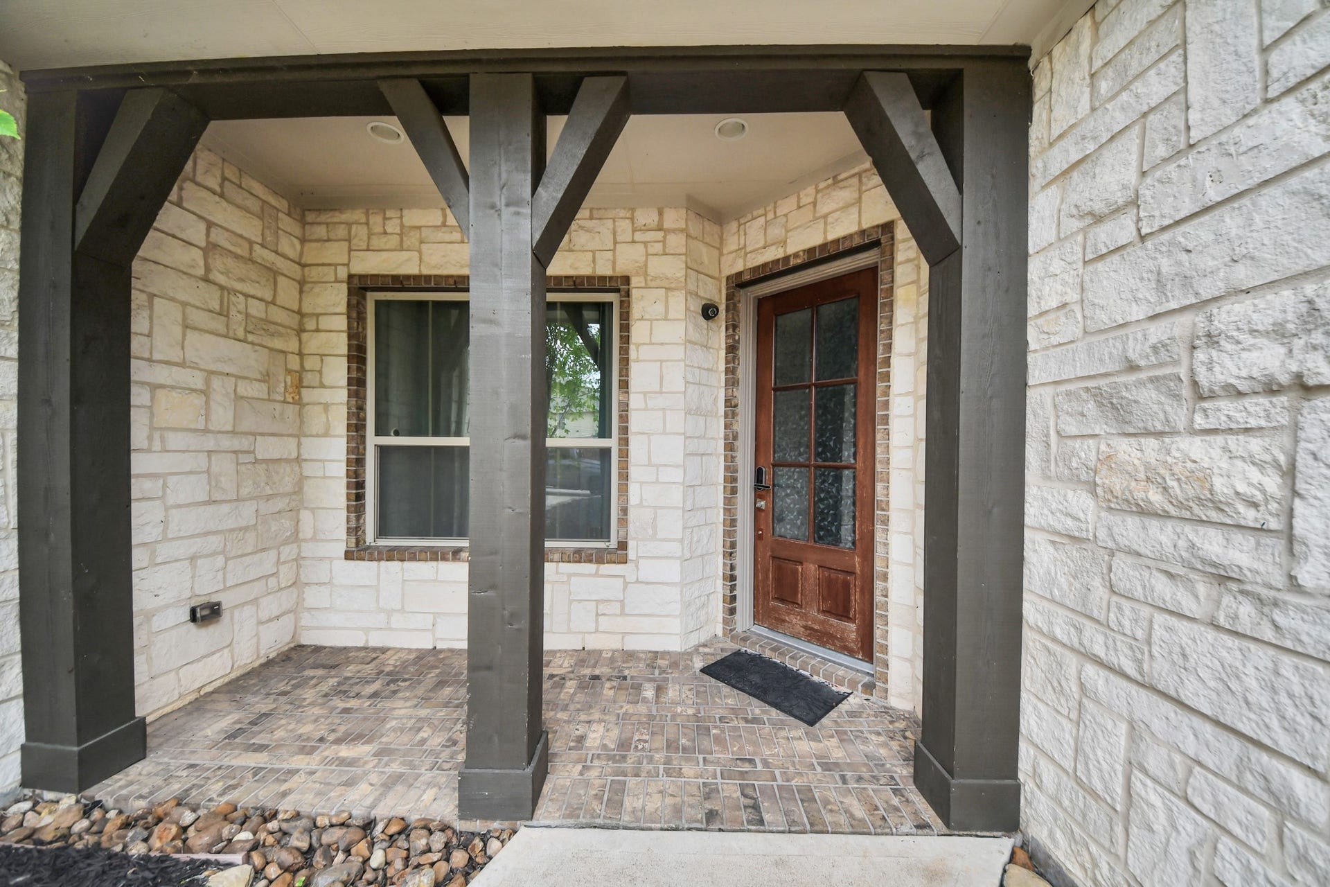 Welcoming covered front porch featuring stone walls, brick flooring, and attractive architectural wood detailing.