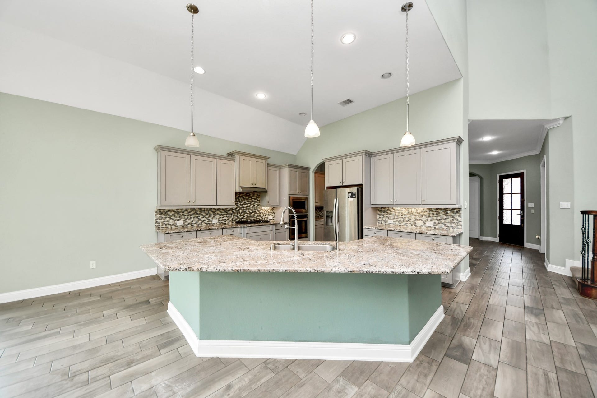 Spacious kitchen featuring an oversized granite island, pendant lighting, abundant cabinetry, stainless steel appliances, and mosaic tile backsplash.