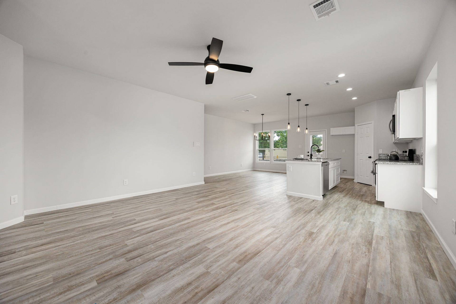 UNIT B- Spacious open-concept living area with modern wood flooring, ceiling fan, and ample natural light. Features a sleek kitchen with an island, pendant lighting, and stainless steel appliances. Ideal for entertaining and family gatherings.