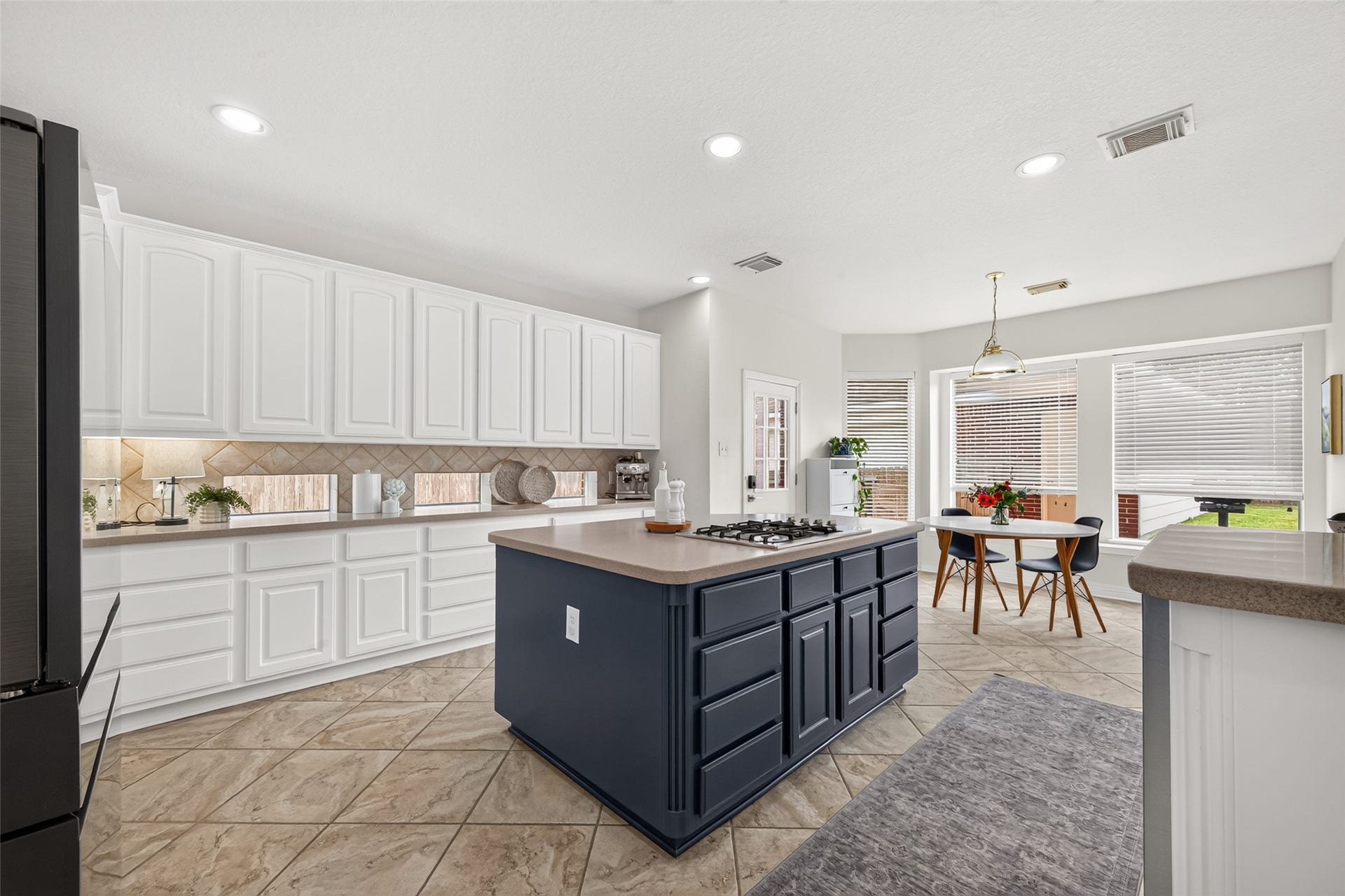 Bright and spacious kitchen featuring sleek white cabinetry, a central island with a cooktop, and a cozy dining area with abundant natural light.