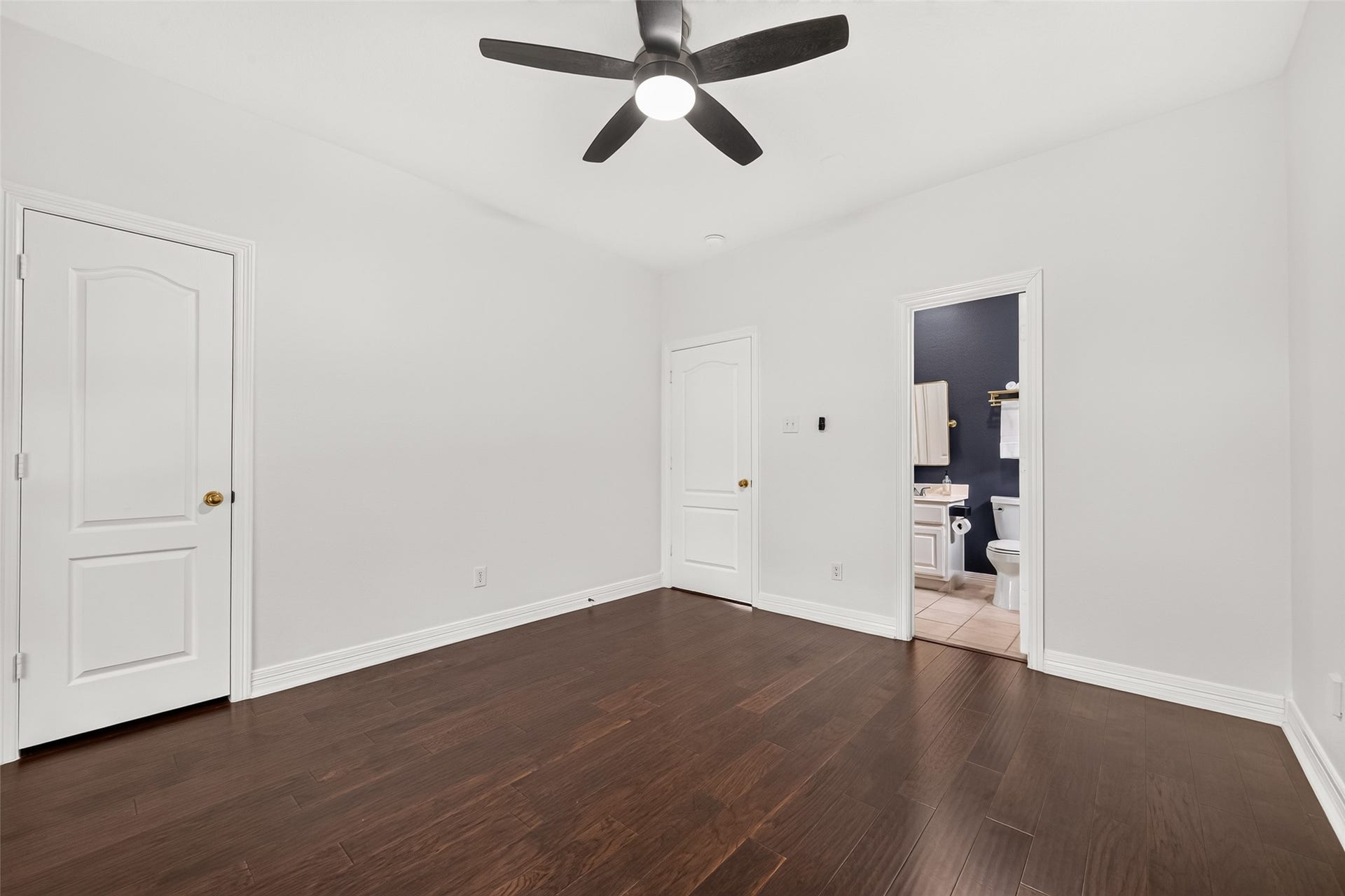 First floor guest bedroom featuring hardwood flooring, ceiling fan, and convenient ensuite bathroom access.