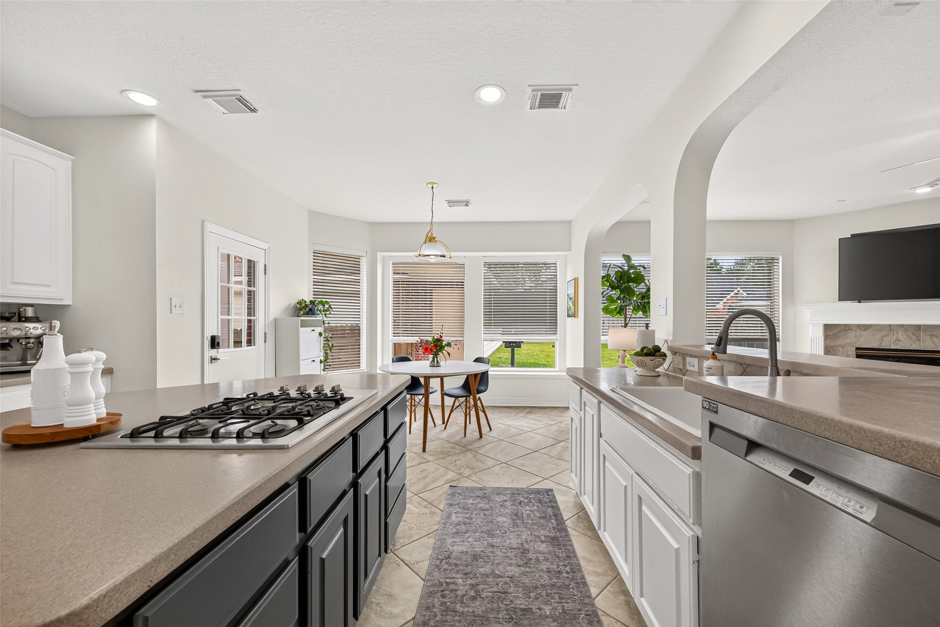Spacious and modern kitchen with sleek countertops, a gas cooktop, and stainless steel appliances. Sunlit dining area with large windows offers a cozy breakfast nook, while the open layout seamlessly connects to the living room featuring a fireplace.