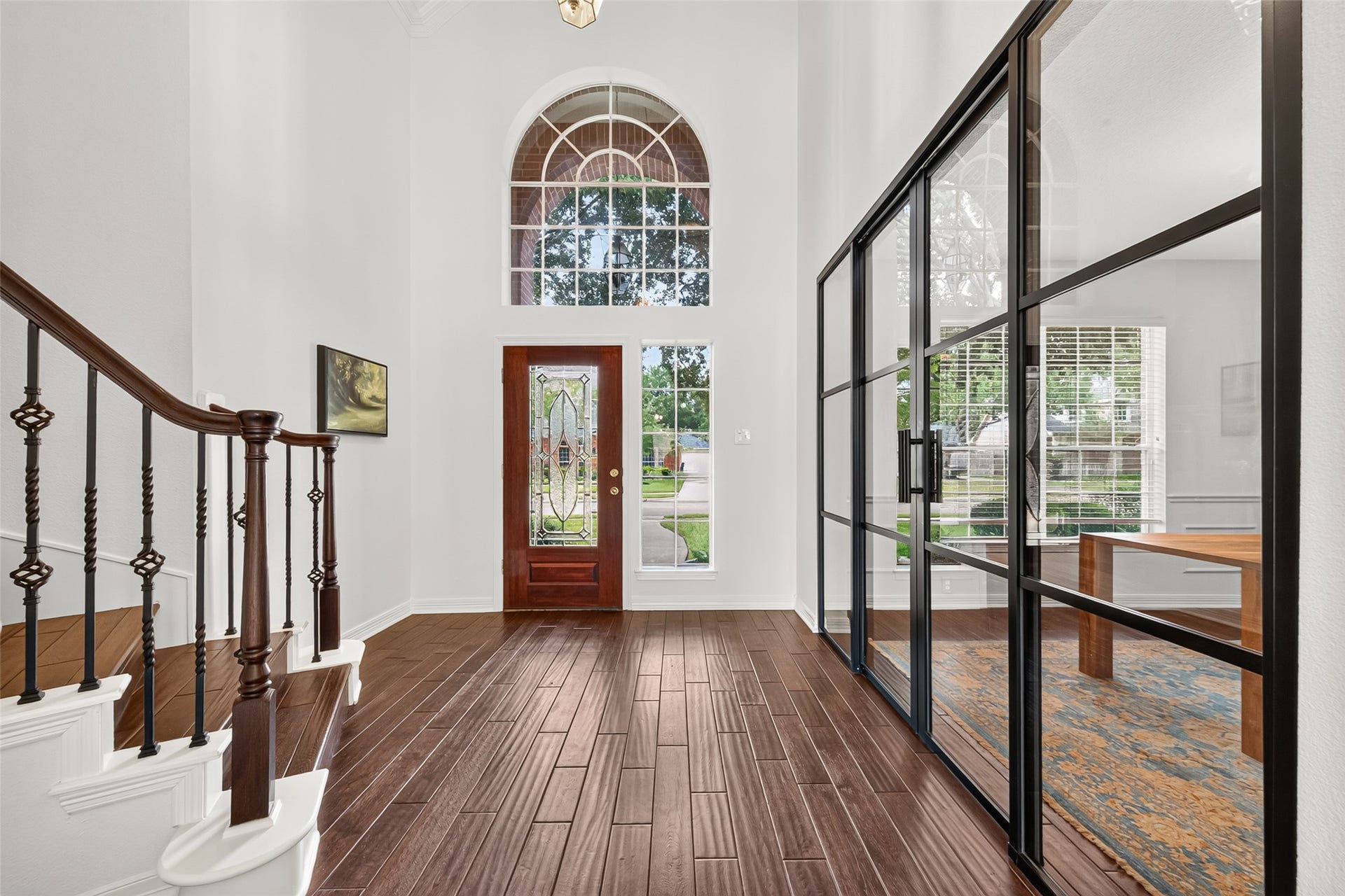 Stunning foyer with high ceilings, elegant staircase, and abundant natural light, complemented by a stylish glass-enclosed office.