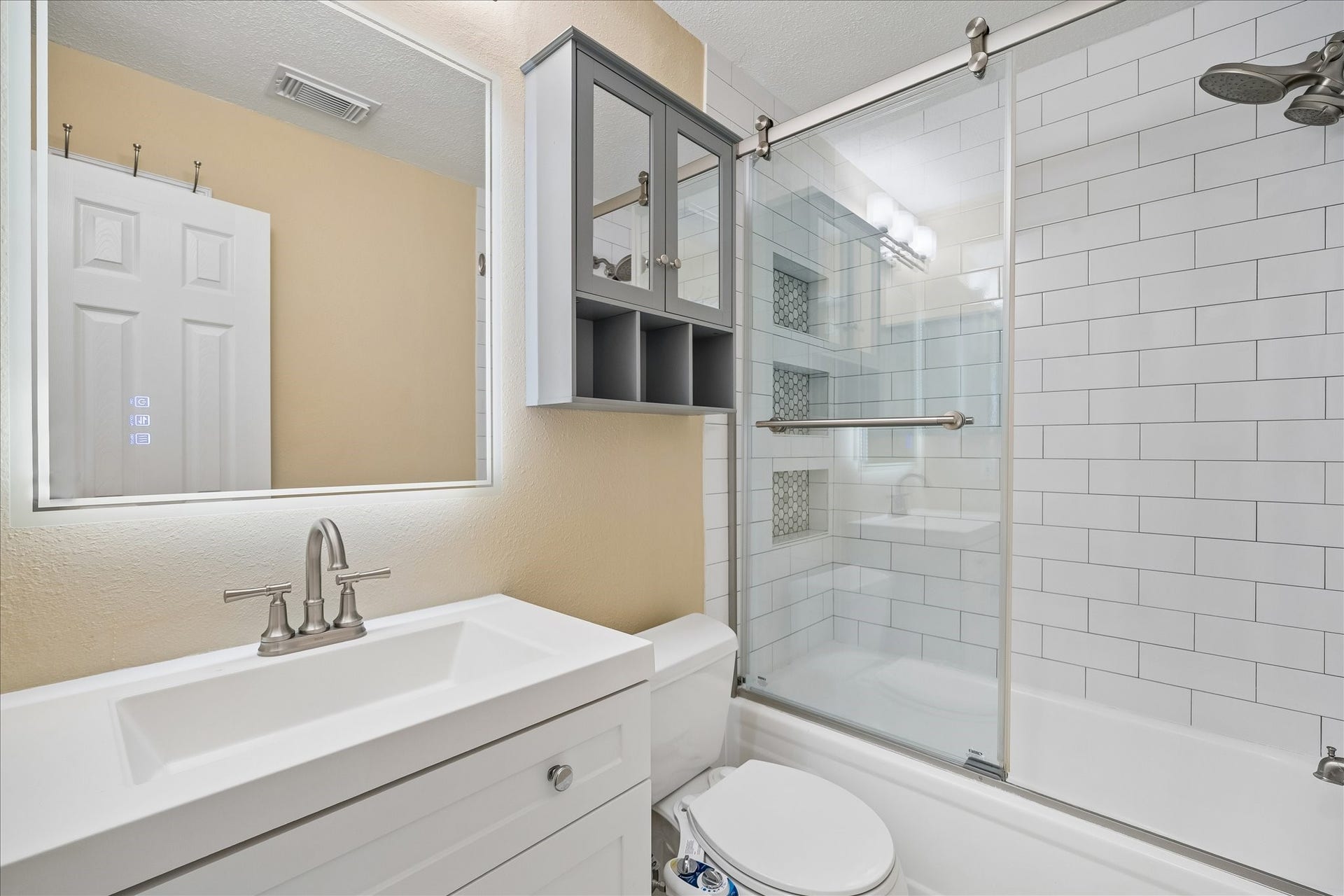 3911 Kitchen Hill Lane, Sugar Land, TX 77479 Enjoy a clean, modern look in this updated bathroom with a white vanity, subway tile, and a glass-enclosed tub and shower.